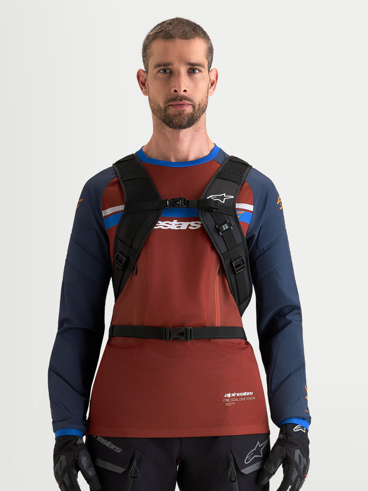 Sac à dos Alpinestars AT-9, sac à dos de motocross noir et gris foncé, vue de face porté par un modèle masculin avec harnais d'épaule rembourré et système de boucle de poitrine