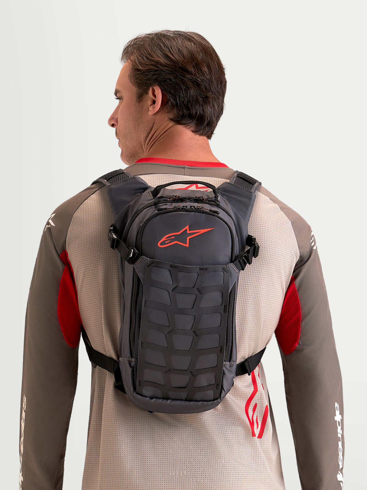 Alpinestars AT-9 Rucksack, Motocross- und Alltagsrucksack an einem Model getragen, Walnuss- und Dunkelgrau, Textilkonstruktion mit organisiertem Stauraum und markantem roten Astar-Logo