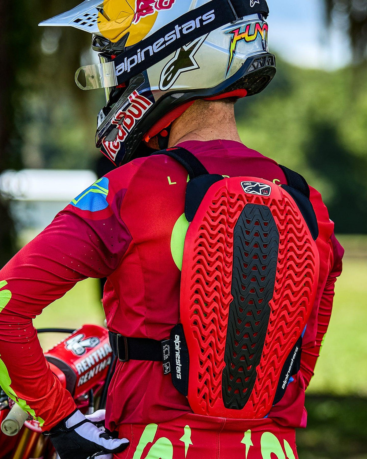 Pilote de motocross vu de dos portant le pare-pierres Alpinestars A-5 Plasma, doté d'une protection dorsale rouge et noire avec une structure alvéolée ventilée, porté sur un maillot rouge à manches longues avec un casque Red Bull.