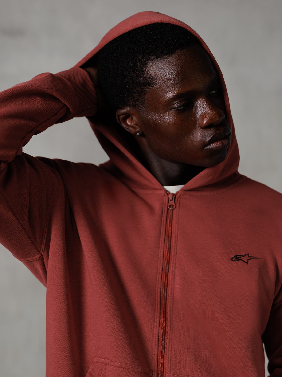 Alpinestars Essentials Ageless Zip Hoodie, Ziegelrot, lässige Lifestyle-Streetwear, aufgesetzte Kapuze mit Hand hinter dem Kopf, kleines schwarzes Astars-Logo auf der Brust, Fleece-Hoodie mit entspannter Passform