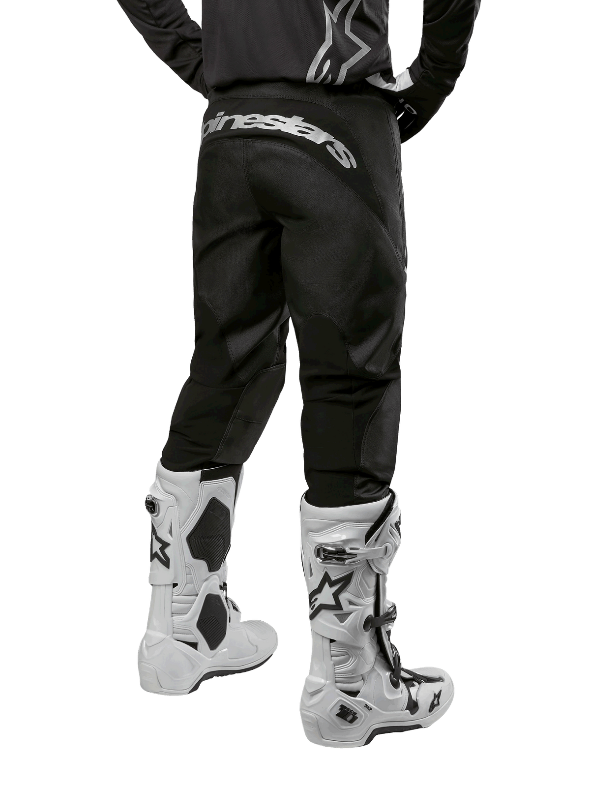 Alpinestars 2024 Fluid Graphite Hose, Motocross-Hose, Schwarz und Silber, Rückansicht mit silbernem Alpinestars-Branding am hinteren Joch, getragen mit weiß-schwarzen Motocross-Stiefeln, strapazierfähiges Textildesign für Offroad-Einsätze