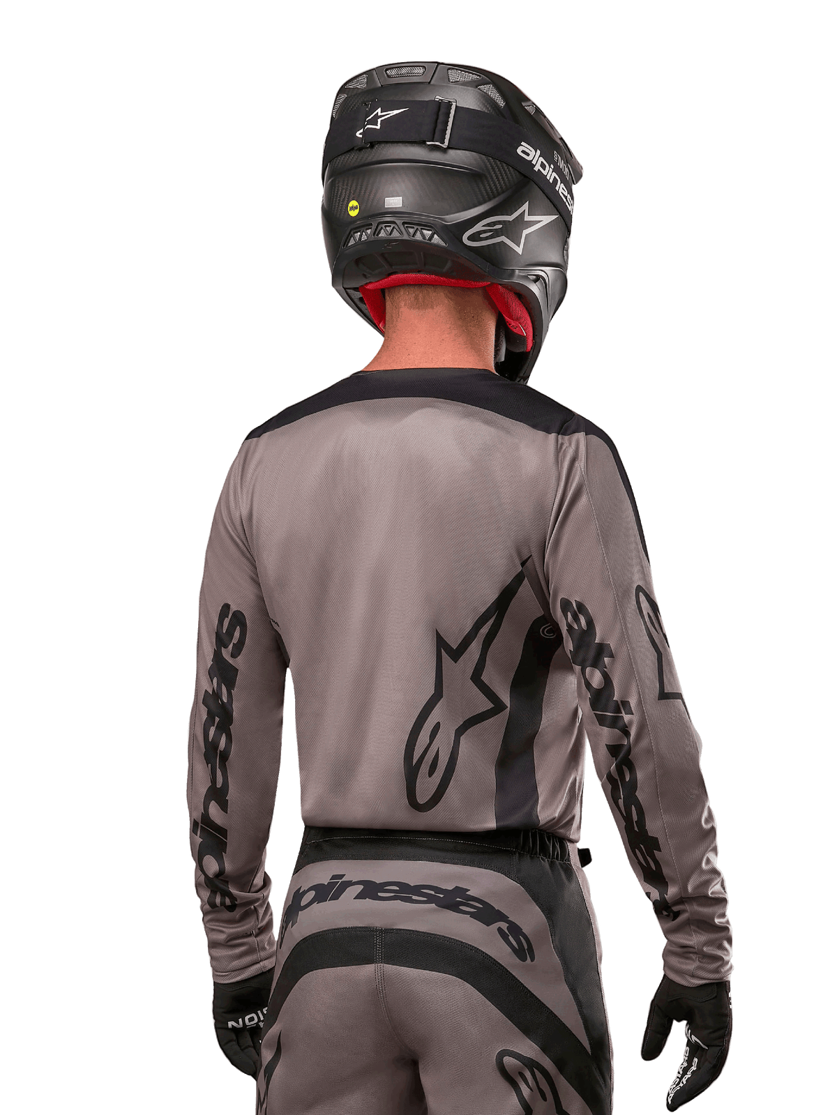 Motocross-Fahrer in der Rückansicht, trägt das Alpinestars 2024 Fluid Lurv Trikot in Mud Black, mit schwarzem Alpinestars-Branding auf Ärmeln und Rücken, kombiniert mit einem schwarzen Helm und passender Ausrüstung für den Offroad-Rennsport