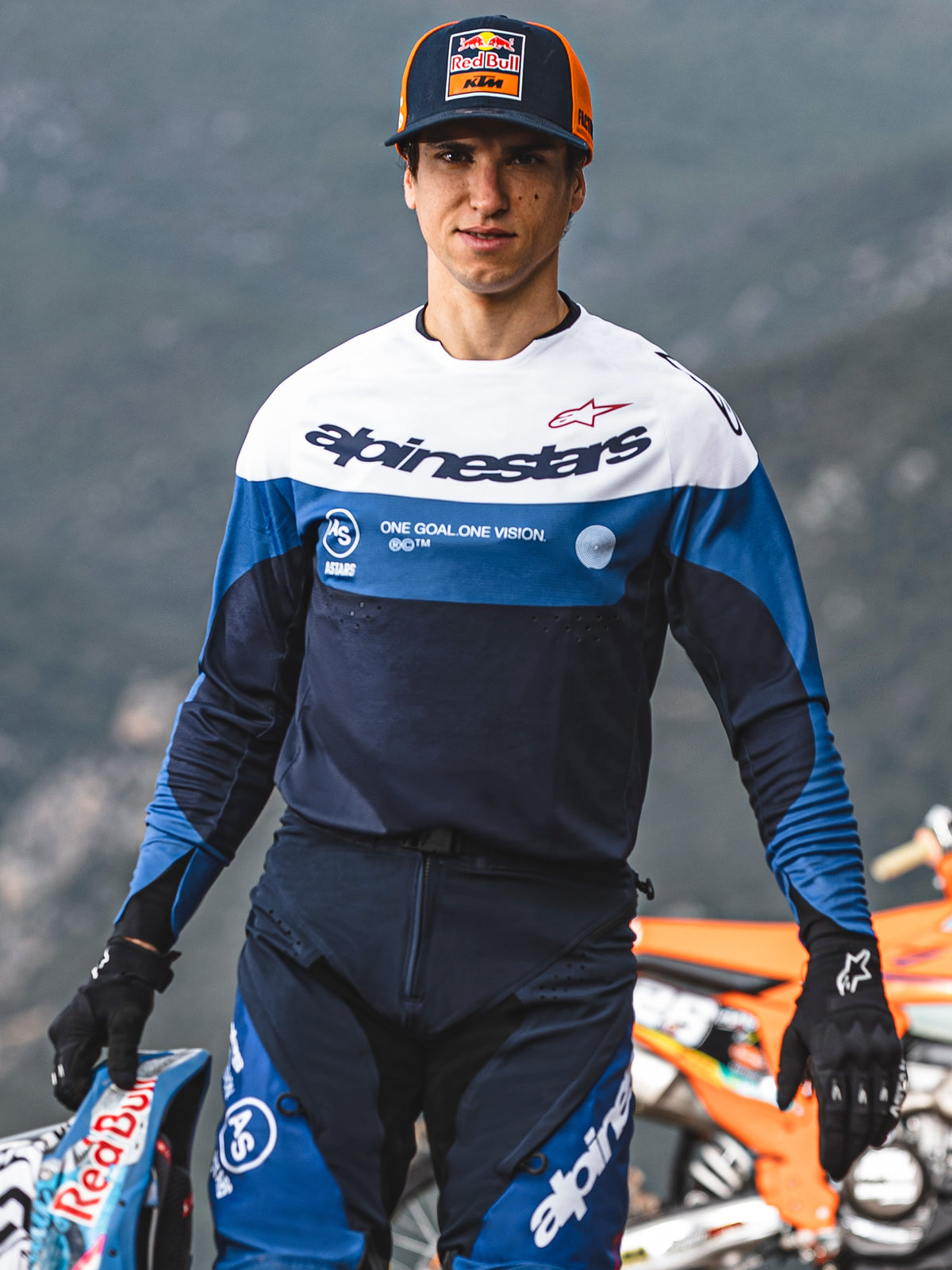 Pilote de motocross portant le maillot Alpinestars Pro-Dura bleu marine, bleu vif et blanc, arborant le logo Alpinestars et le slogan « One Goal. One Vision. », avec un équipement assorti et une casquette Red Bull KTM en extérieur.