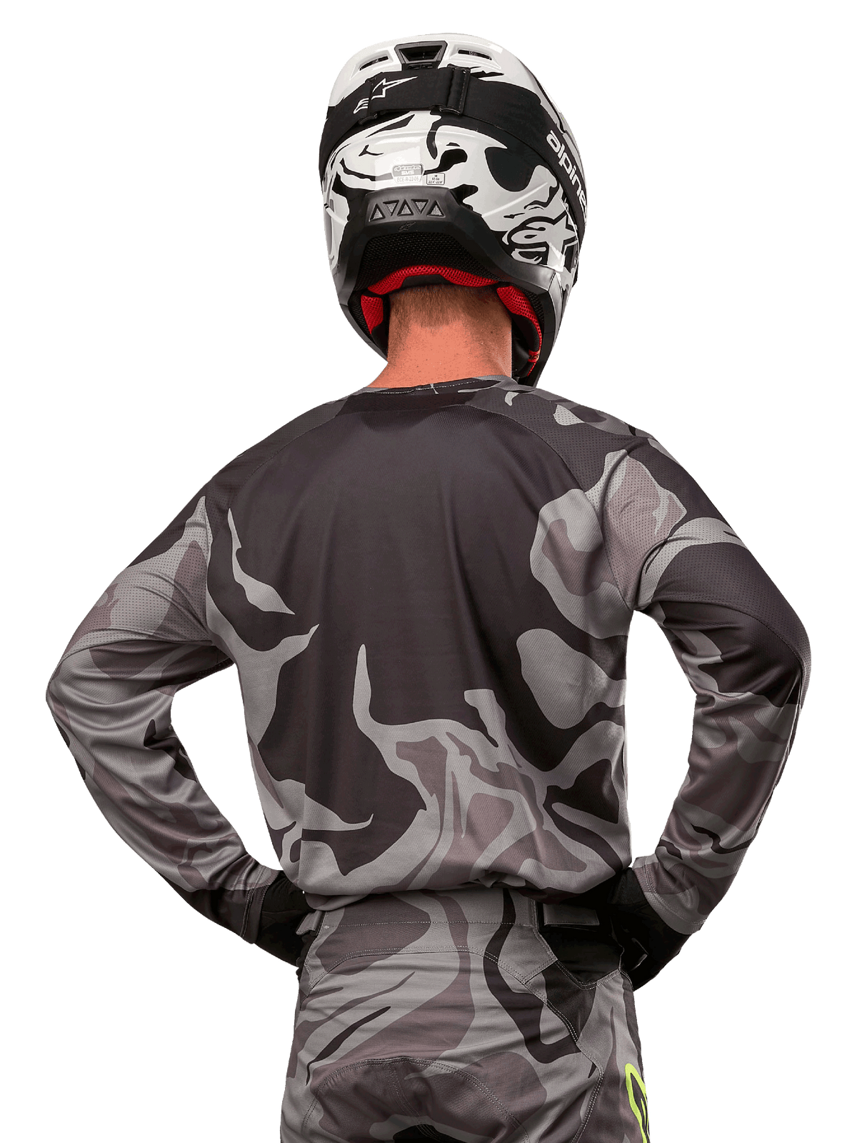 Maillot Alpinestars Racer Tactical 2024, maillot de motocross, Cast Gray Camo Magnet, vue arrière montrant un motif camouflage gris et noir, porté avec un pantalon assorti et un casque noir et blanc, équipement de course tout-terrain professionnel