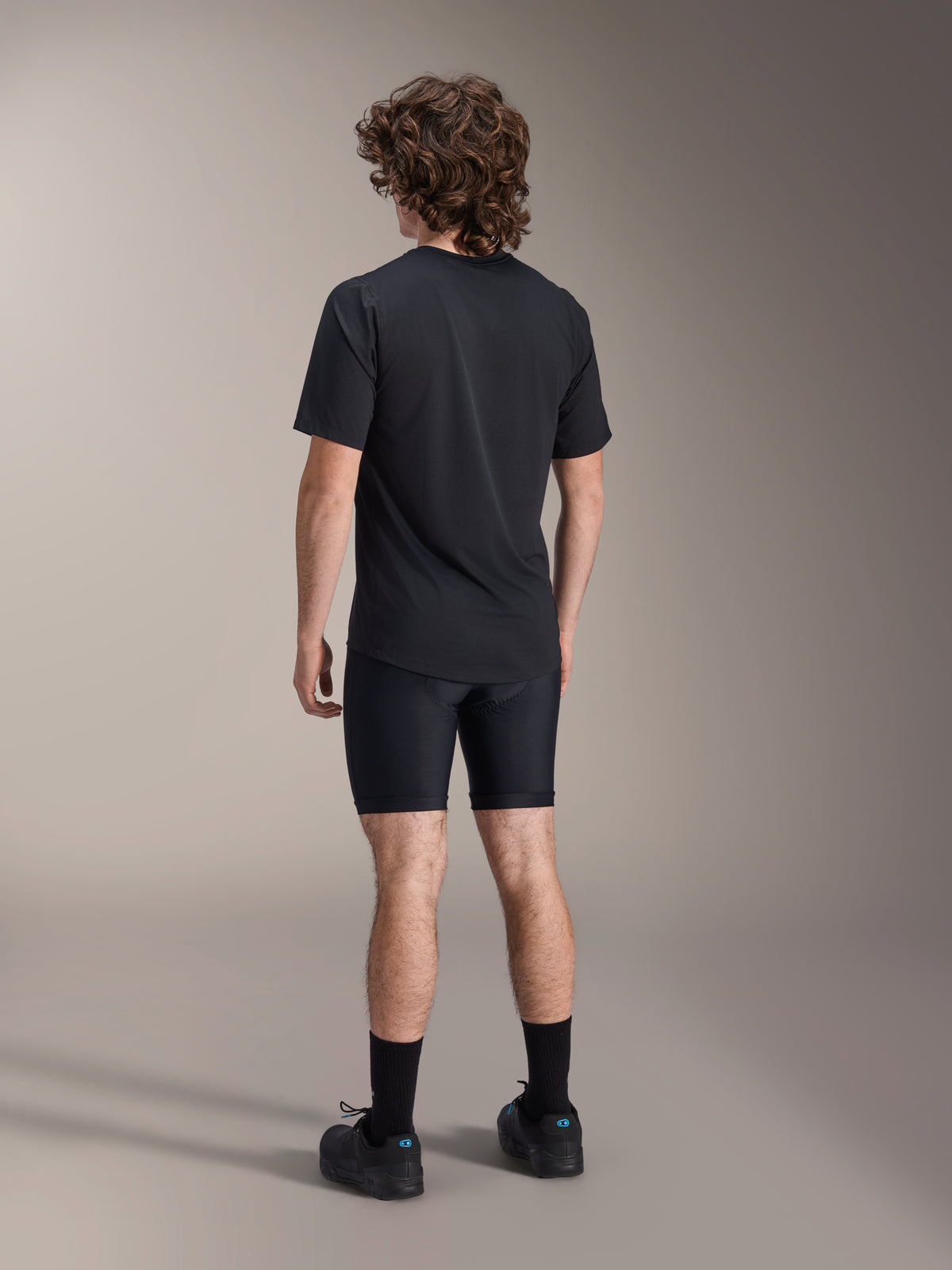 Alpinestars A-Dura Liner Shorts, zwarte fiets-linershorts, achteraanzicht op model, nauwsluitende stretchstof met zichtbare naden van de zeemvulling, gecombineerd met een zwart t-shirt en fietsschoenen, mountainbikekleding
