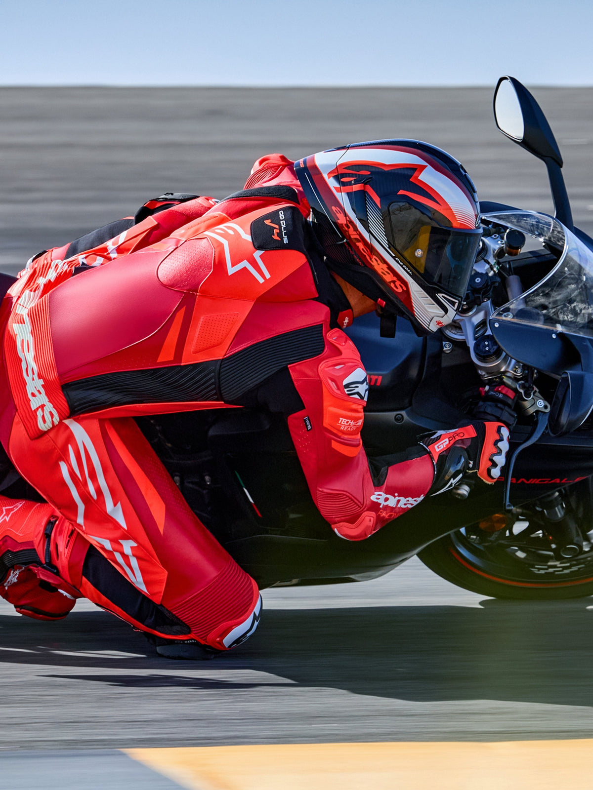 Alpinestars GP Plus V4 Sprint Lederkombi, Tech-Air® Ready, Fluo-Rot und Weiß, Motorradfahrer in Schräglage auf Rennstrecke.