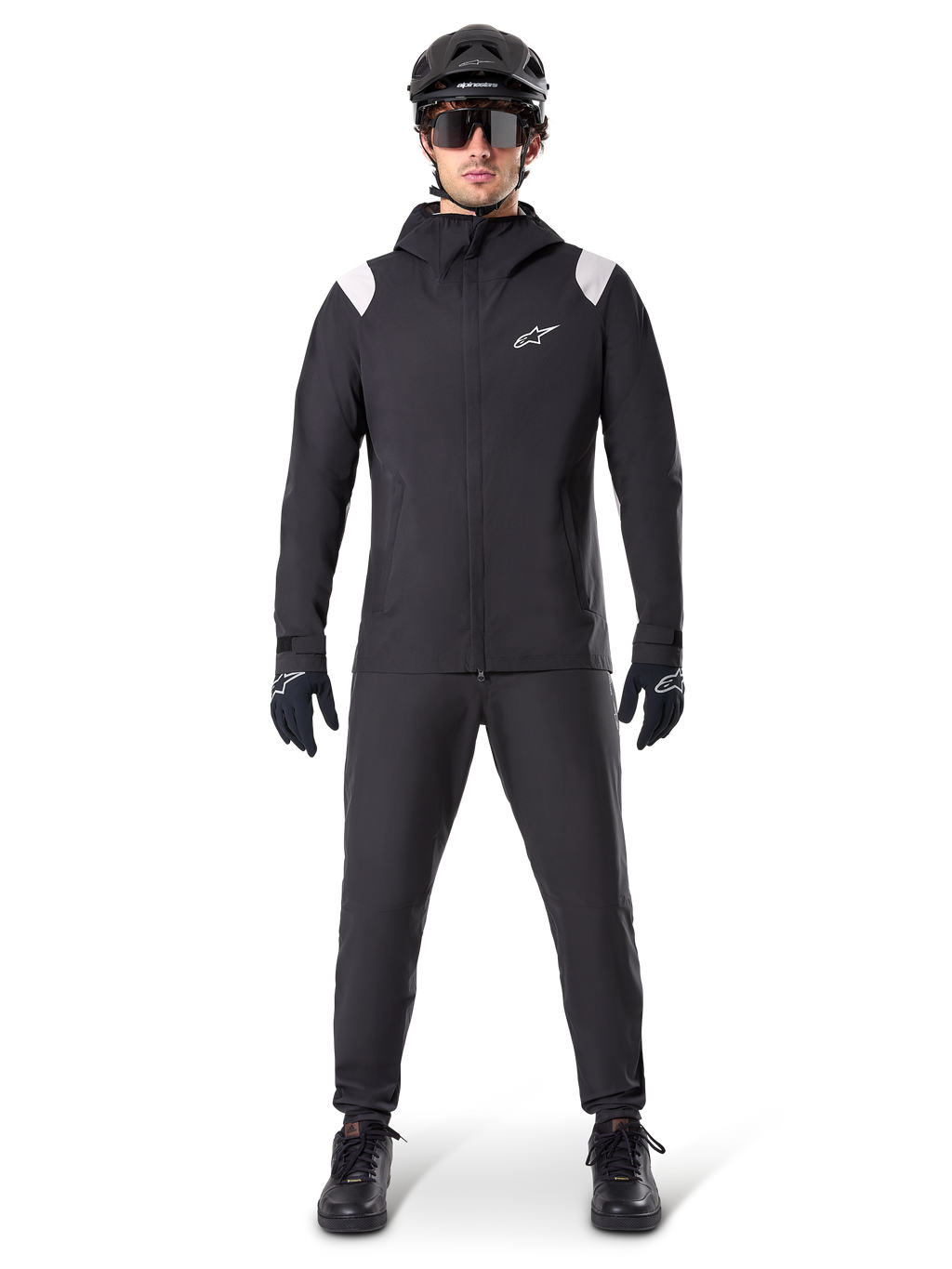 Veste de pluie Alpinestars A-Dura, veste de pluie de VTT, noire avec accents blancs aux épaules et logo blanc sur la poitrine, portée avec pantalon noir, casque noir, lunettes de soleil et gants, équipement de VTT coordonné pour le temps pluvieux