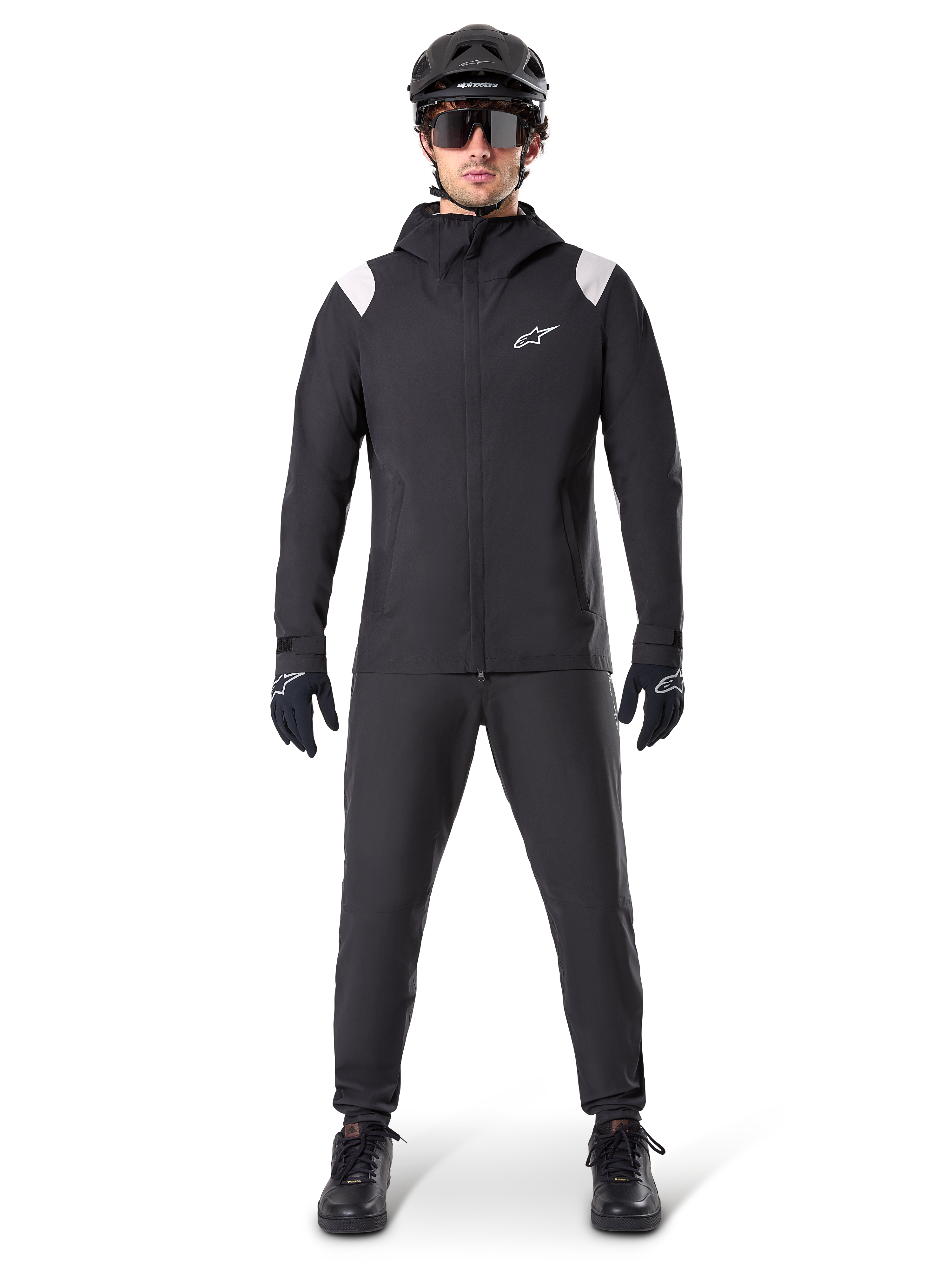 Veste de pluie Alpinestars A-Dura, veste de pluie de VTT, noire avec accents blancs aux épaules et logo blanc sur la poitrine, portée avec pantalon noir, casque noir, lunettes de soleil et gants, équipement de VTT coordonné pour le temps pluvieux
