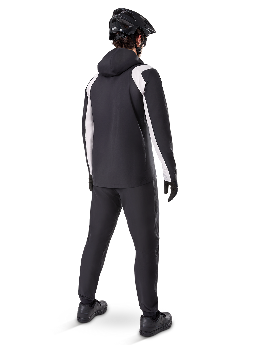Veste de pluie Alpinestars A-Dura, vue arrière d'un cycliste portant la veste de VTT imperméable noire et blanche, pantalon de cyclisme noir assorti, casque et gants noirs, équipement technique pour le VTT par conditions humides