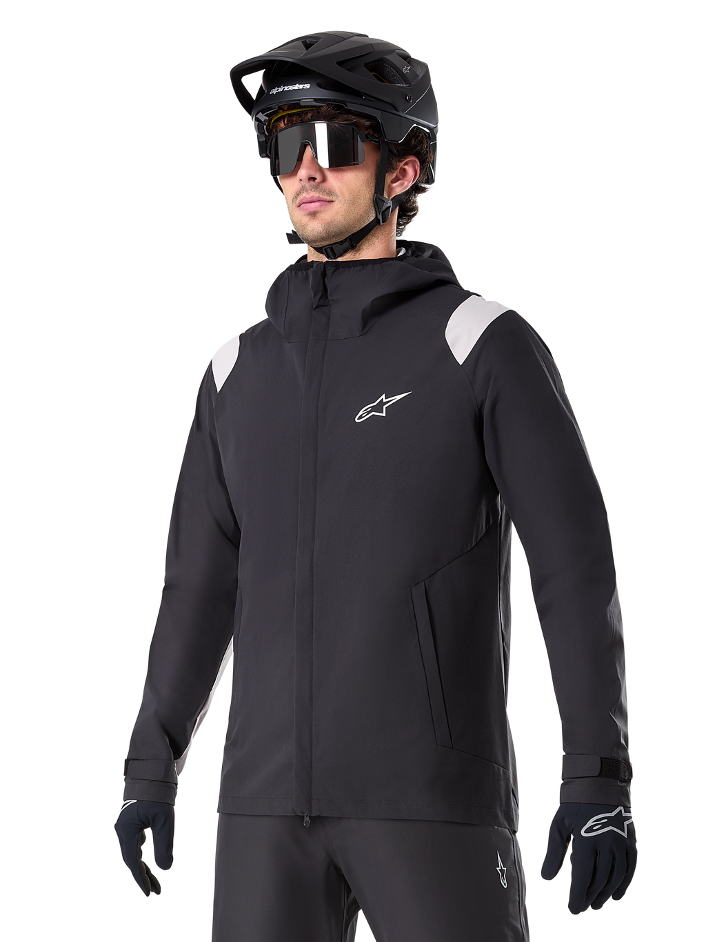 Veste de pluie Alpinestars A-Dura, veste de pluie pour VTT, noire avec accents gris clair sur les épaules, portée par un cycliste avec un casque de VTT noir et des lunettes de soleil, logo blanc sur la poitrine, construction imperméable, coordonnée avec un pantalon et des gants noirs pour le cyclisme tout-terrain