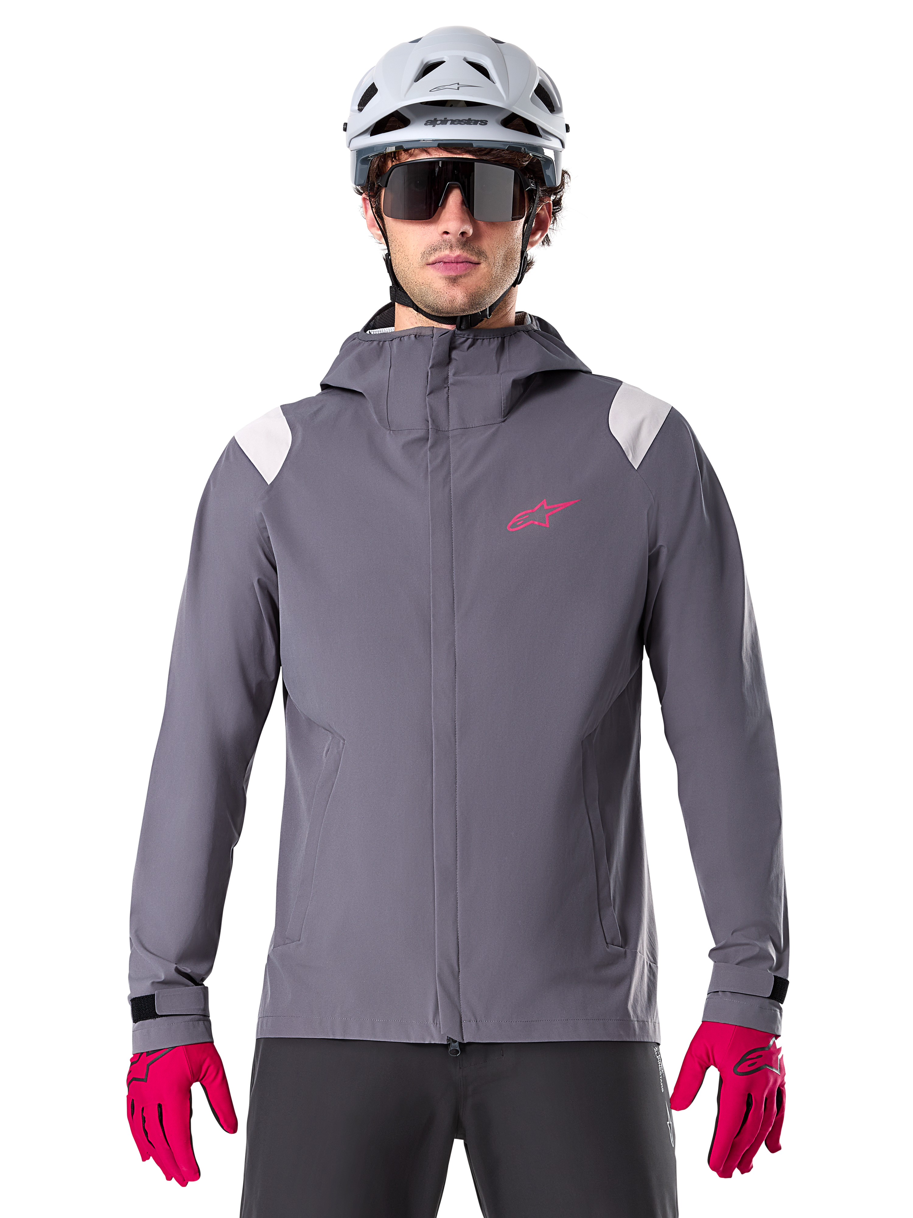 Veste de pluie Alpinestars A-Dura, veste de pluie pour VTT, gris titanium foncé, modèle à capuche avec logo Alpinestars rose et empiècements gris clair aux épaules, portée avec un casque de VTT blanc et des gants rose vif, équipement imperméable pour le cyclisme tout-terrain