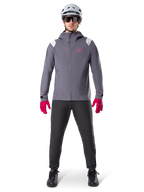 Veste de pluie Alpinestars A-Dura, veste de VTT, gris titane foncé avec logo rose, portée avec un casque de VTT gris et des gants rose vif, membrane protectrice à 2,5 couches pour le cyclisme par temps humide
