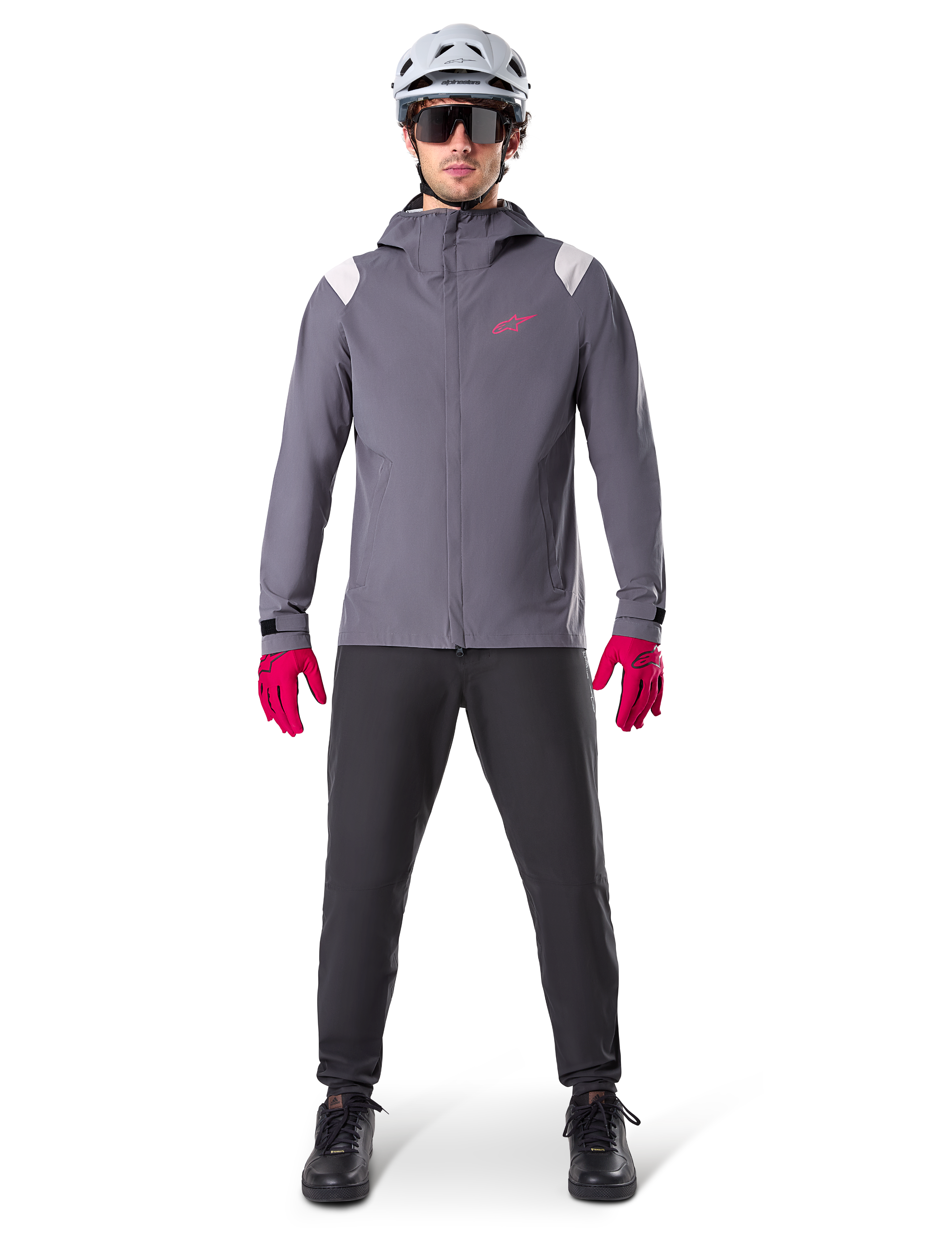 Veste de pluie Alpinestars A-Dura, veste de VTT, gris titane foncé avec logo rose, portée avec un casque de VTT gris et des gants rose vif, membrane protectrice à 2,5 couches pour le cyclisme par temps humide