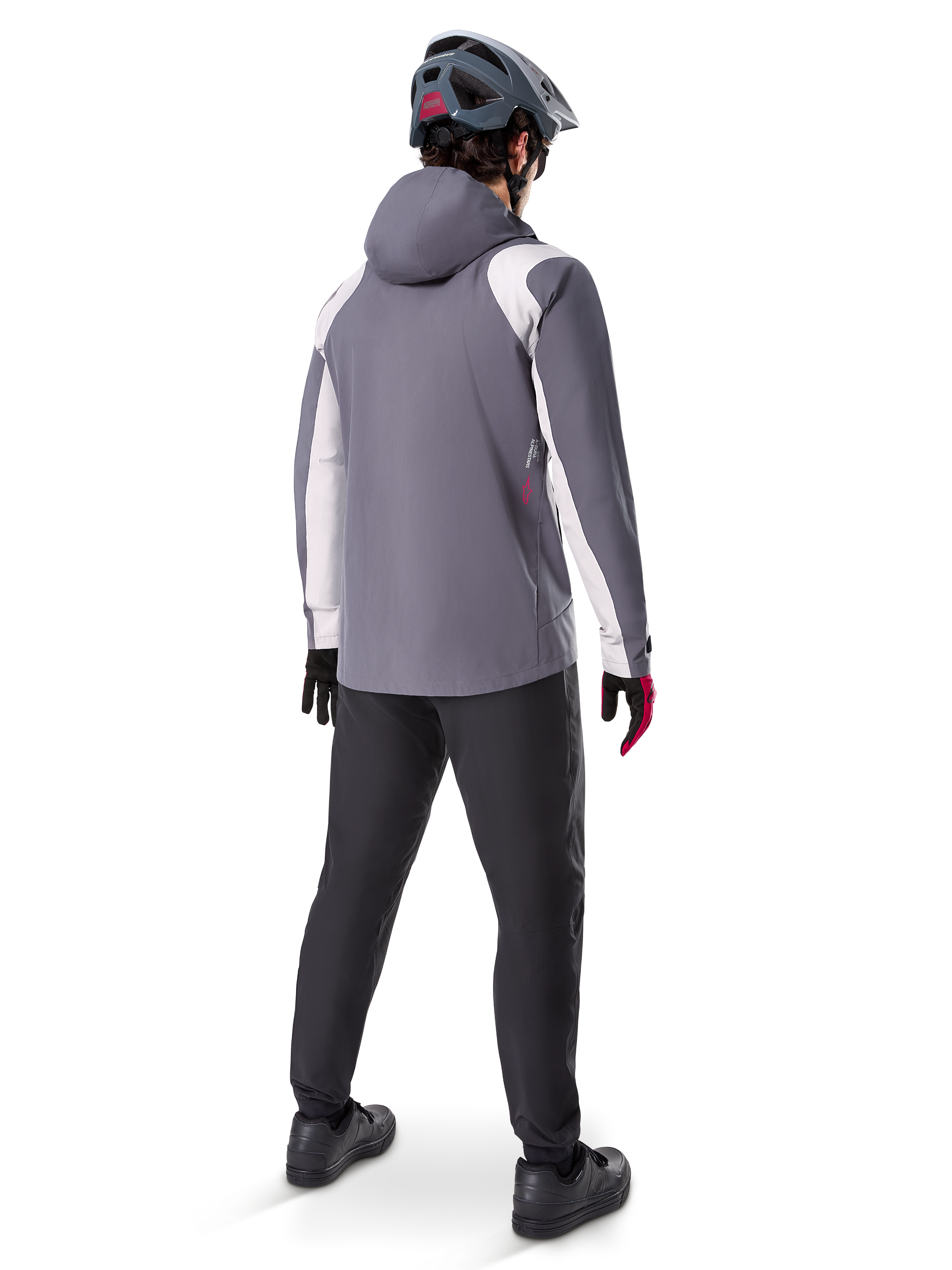 Veste de pluie Alpinestars A-Dura, veste de VTT, gris titane foncé avec empiècements blancs, vue arrière d'un cycliste portant un casque gris assorti et un pantalon noir, équipement technique pour temps humide