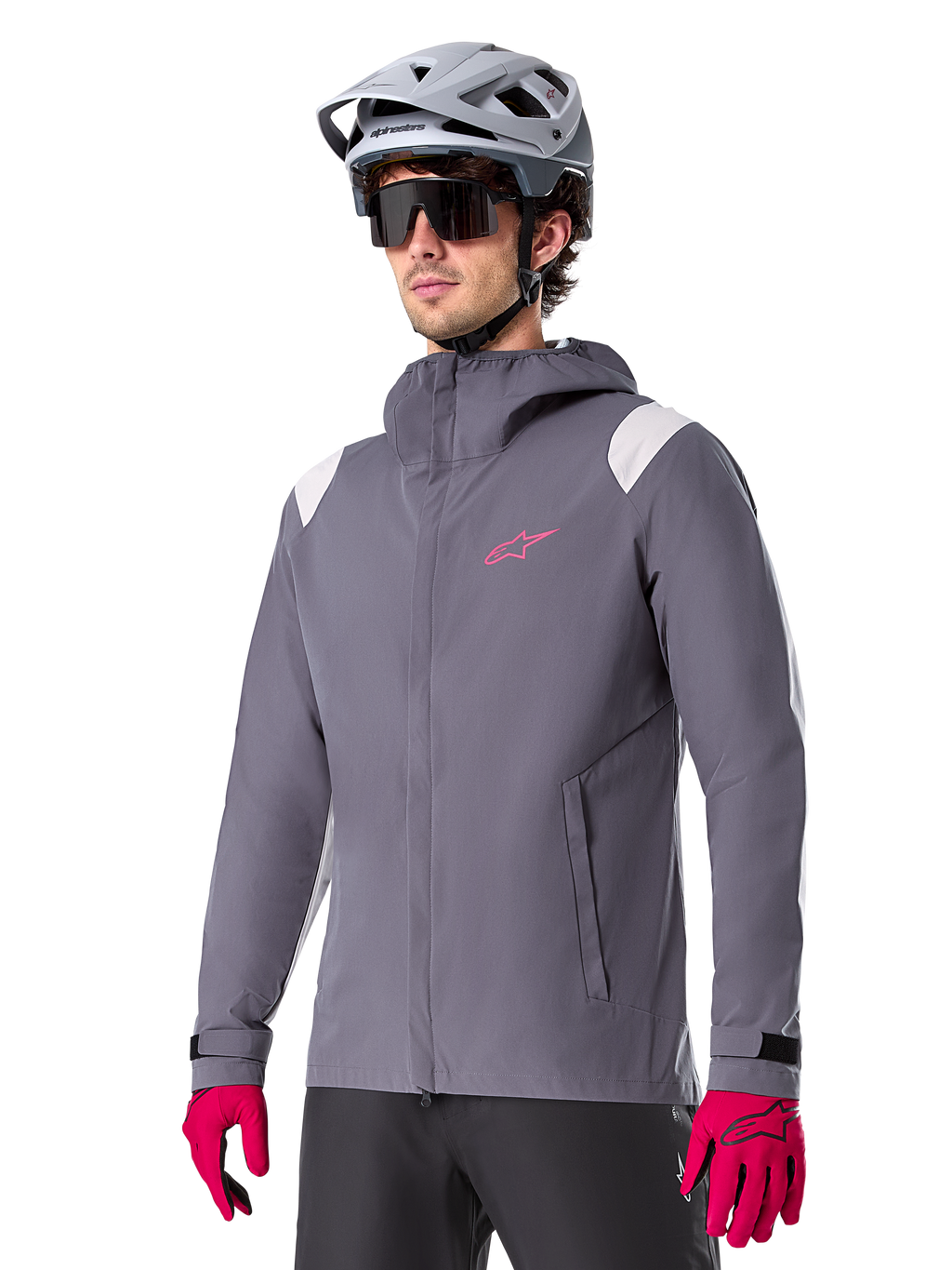 Veste de pluie Alpinestars A-Dura, veste de pluie pour VTT, gris titane foncé avec logo rose et accents blancs sur les épaules, modèle à capuche avec poches avant, portée avec des gants roses et un casque de vélo gris clair