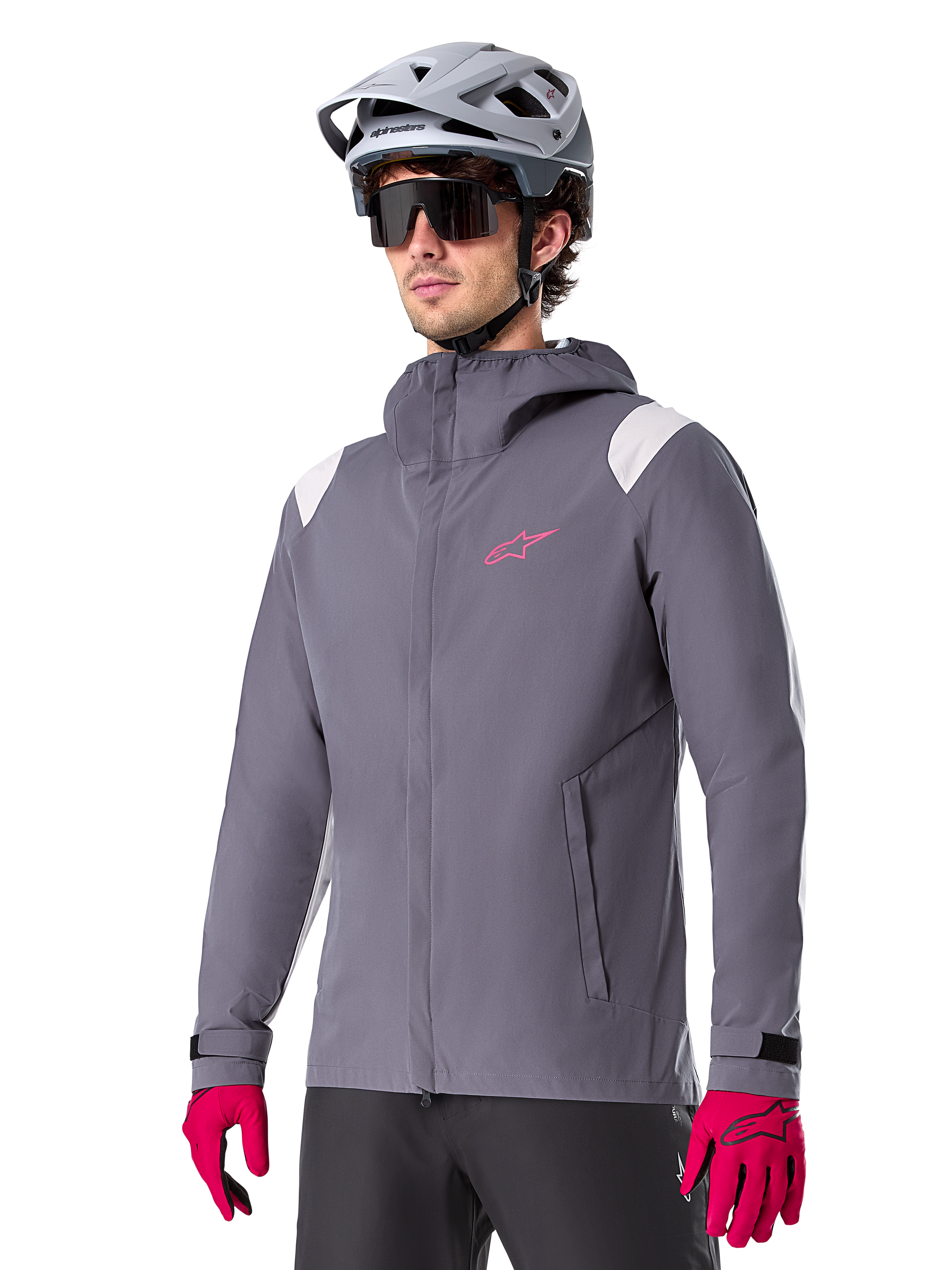 Alpinestars A-Dura Regenjas, mountainbike-regenjas, donker titanium grijs met roze logo en witte schouderaccenten, ontwerp met capuchon en voorzakken, gedragen met roze handschoenen en een lichtgrijze fietshelm
