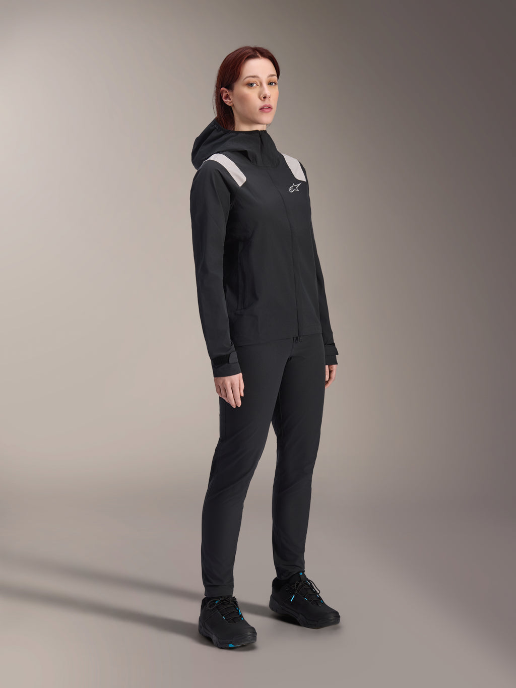 Veste de pluie Alpinestars Stella A-Dura pour femme, noir, membrane VTT imperméable 2,5 couches avec détails gris clair aux épaules, pantalon noir et chaussures de cyclisme assortis, portrait en studio pour équipement de cyclisme haute performance