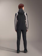 Cycliste vue de dos portant la veste de pluie Alpinestars Stella A-Dura, noire avec des empiècements gris clair sur les manches et les épaules, capuche relevée, portée avec un pantalon noir et des chaussures de cyclisme, équipement technique de pluie pour le VTT