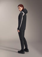 Veste de pluie Alpinestars Stella A-Dura pour femme, noire avec une bande gris clair sur la manche, veste de cyclisme imperméable à capuche pour le VTT, associée à un pantalon technique noir et des chaussures de vélo noires, vue de profil en studio