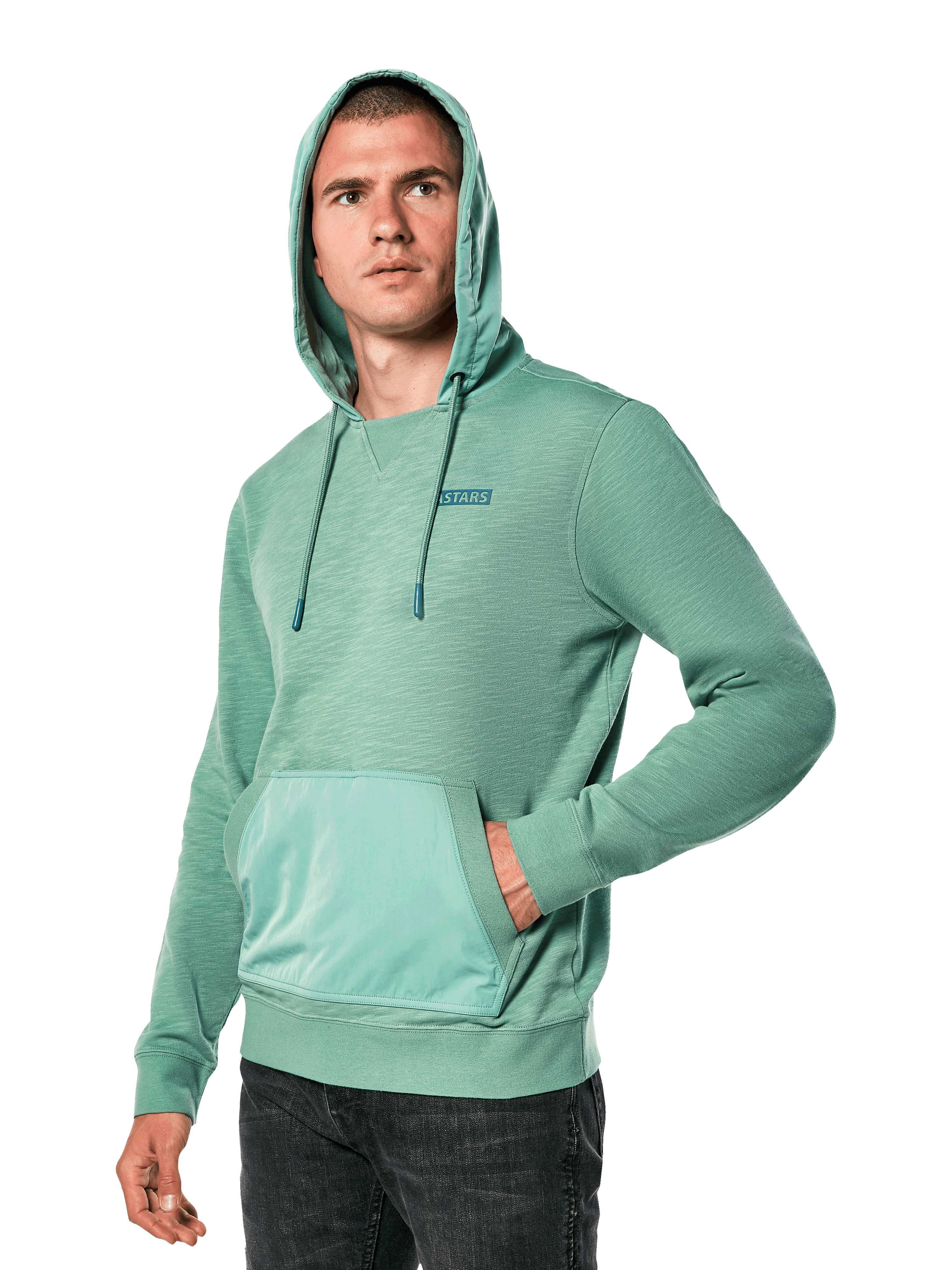 Alpinestars Rooted Hoodie, sweat-shirt vert en molleton flammé avec capuche superposée et poche kangourou, petit logo STARS sur la poitrine, porté par un mannequin avec la capuche relevée et une main dans la poche, style streetwear décontracté d'inspiration sport automobile
