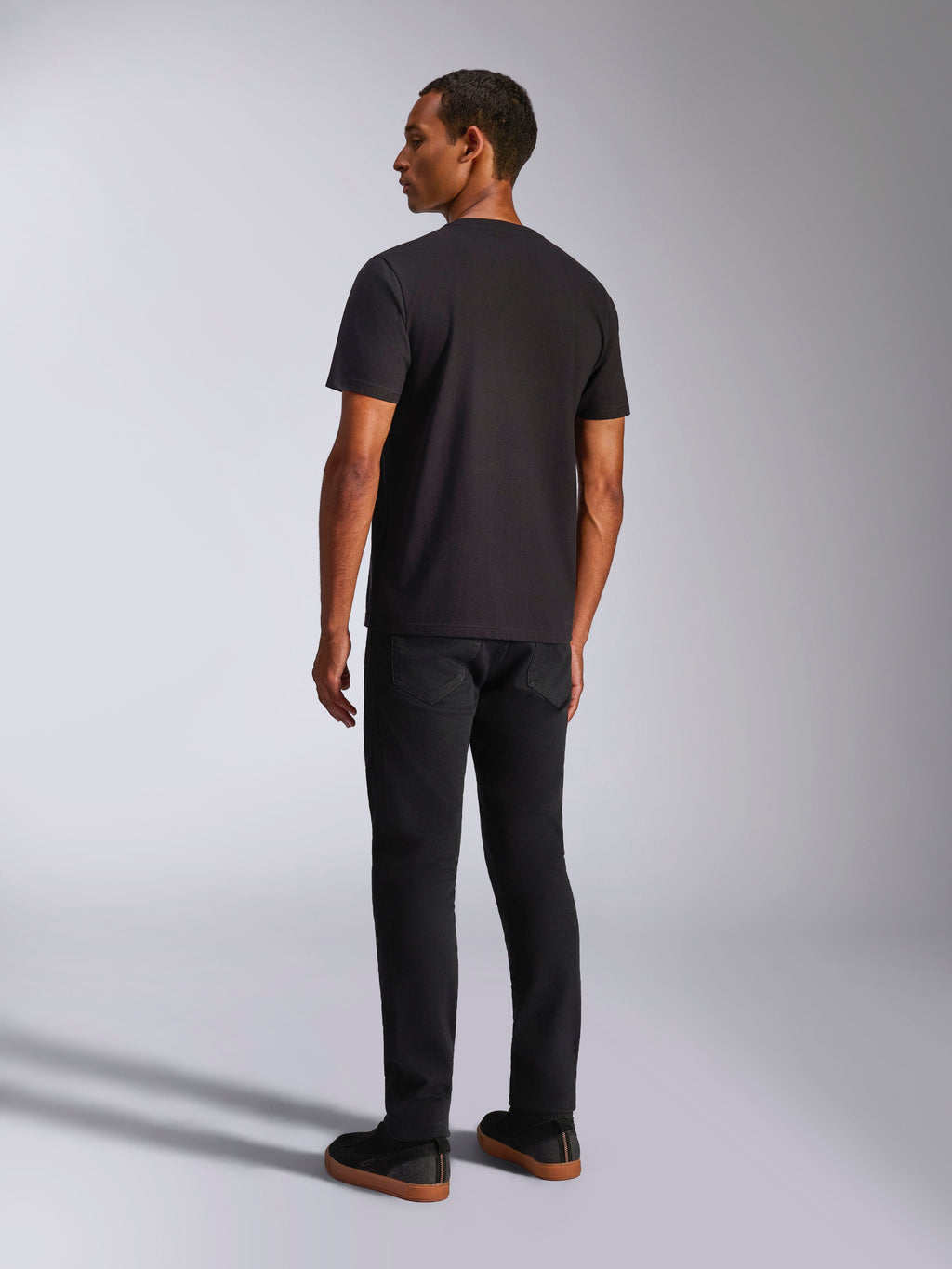 Alpinestars Ageless 2.0 CSF Tee, T-shirt met korte mouwen, zwart, achteraanzicht op een mannelijk model, gedragen met een zwarte broek en sneakers met gomzolen, casual motorsport-geïnspireerde streetwear