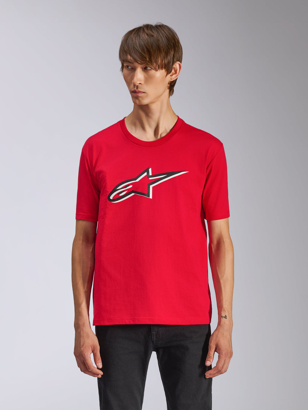 Alpinestars Ageless Shadow CSF Tee, rood T-shirt met korte mouwen, voorzien van een Ageless-logo op de voorkant met zwarte en witte contouren, gedragen door een man met een zwarte broek, casual motorsport streetwear