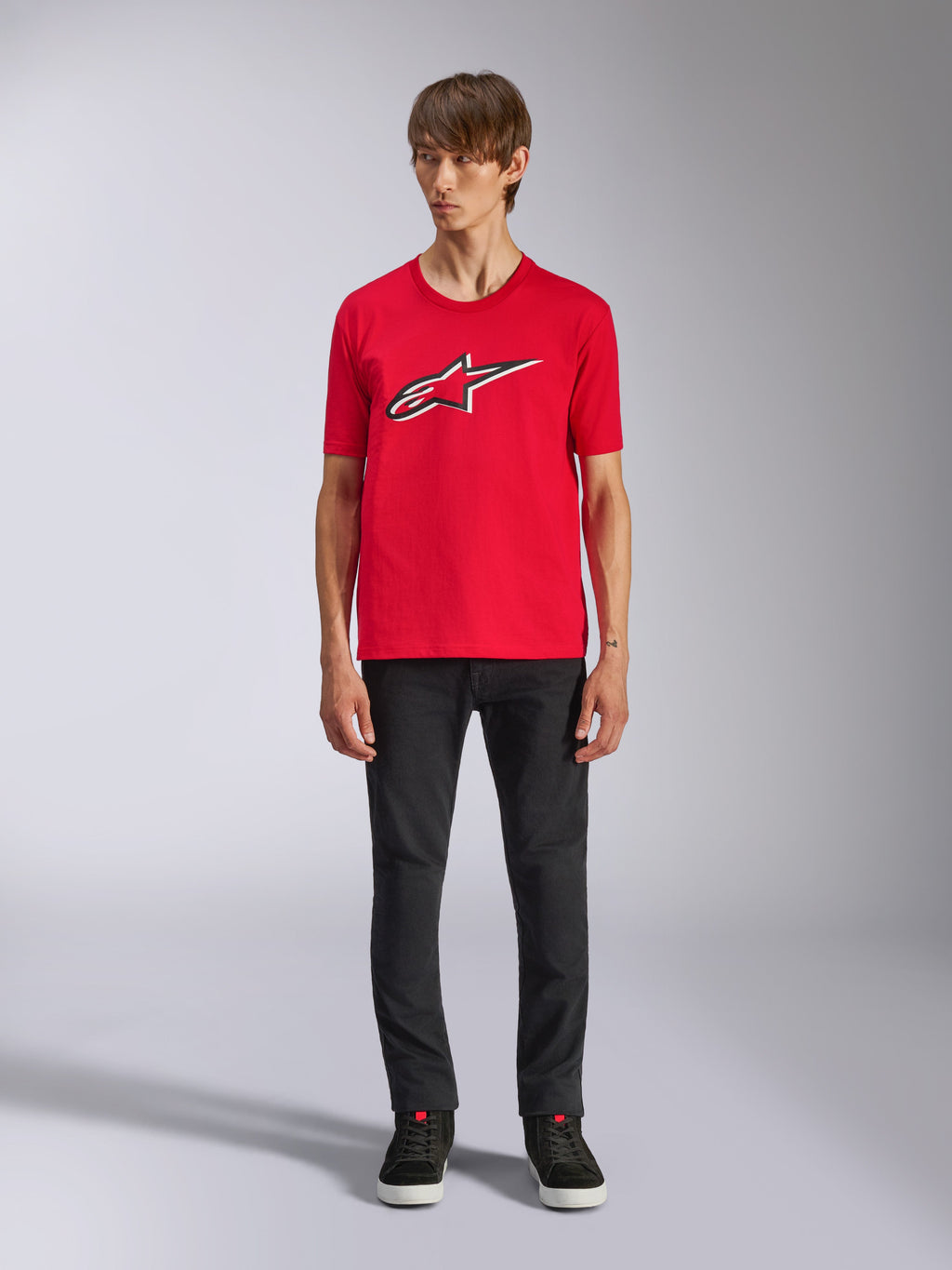 Alpinestars Ageless Shadow CSF Tee, T-shirt met korte mouwen, rood, Ageless-logo op de voorzijde met witte en zwarte contouren, gedragen door een model met zwarte broek en sneakers, casual motorsport streetwear