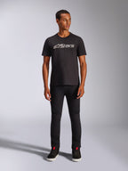 Alpinestars Blaze 2.0 CSF Tee, T-shirt met korte mouwen, zwart met grijs en wit logo op de voorzijde, gedragen door model met zwarte broek en zwarte schoenen, casual streetwear geïnspireerd op motorsport