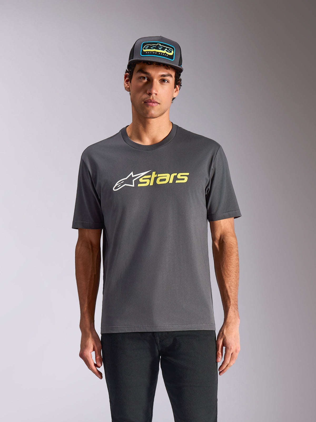 Alpinestars Blaze 2.0 CSF Tee, Kurzarm-T-Shirt, Anthrazitgrau, weißes Stern-Logo und neongelbe „stars“-Grafik, kombiniert mit passender Trucker-Cap und schwarzer Hose, lässige Motorsport-Streetwear