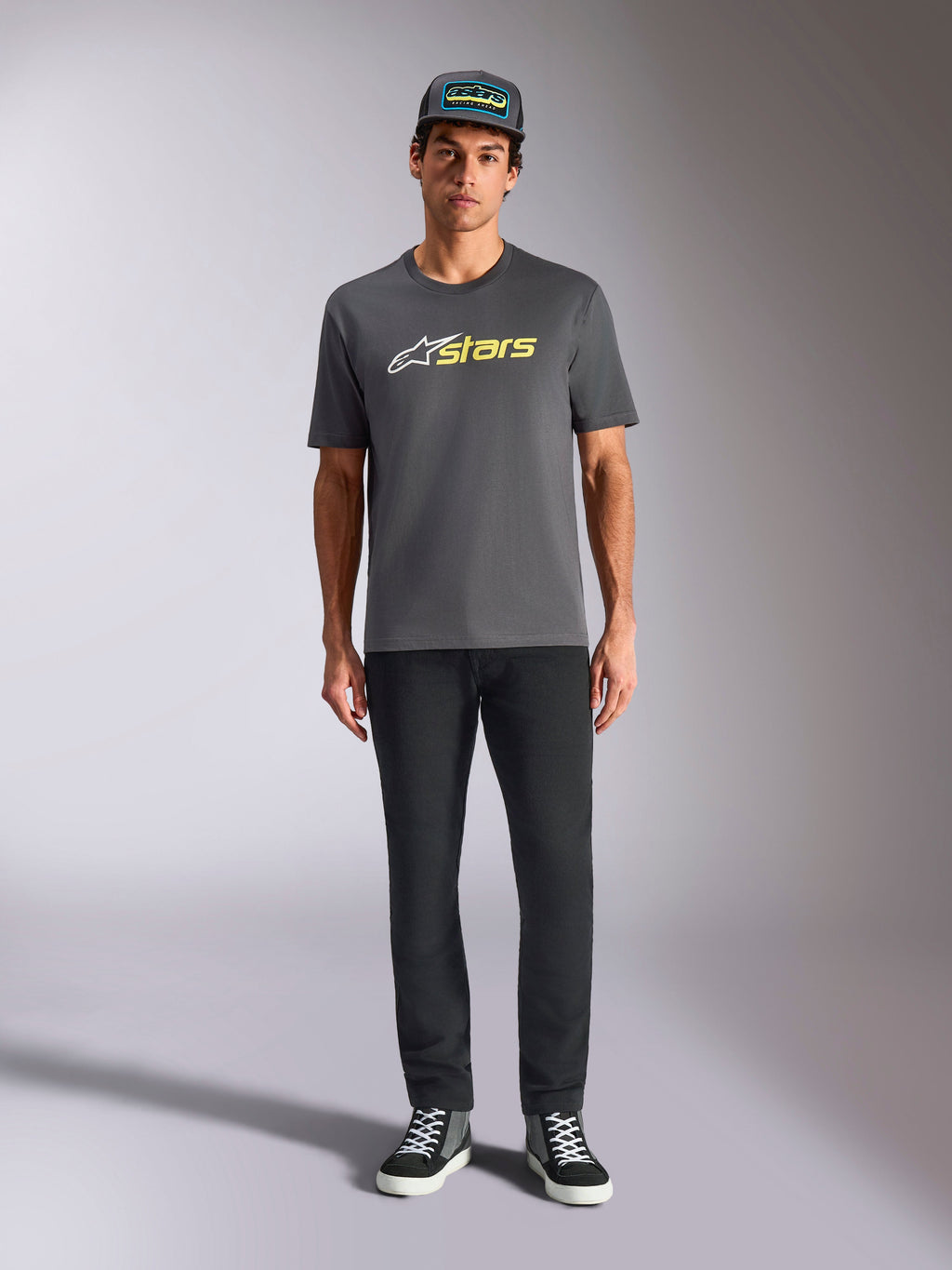 Alpinestars Blaze 2.0 CSF Tee, t-shirt met korte mouwen, antracietgrijs met wit en hi-vis geel logo, gedragen met een zwarte broek en een bijpassende truckerpet, casual motorsport lifestyle