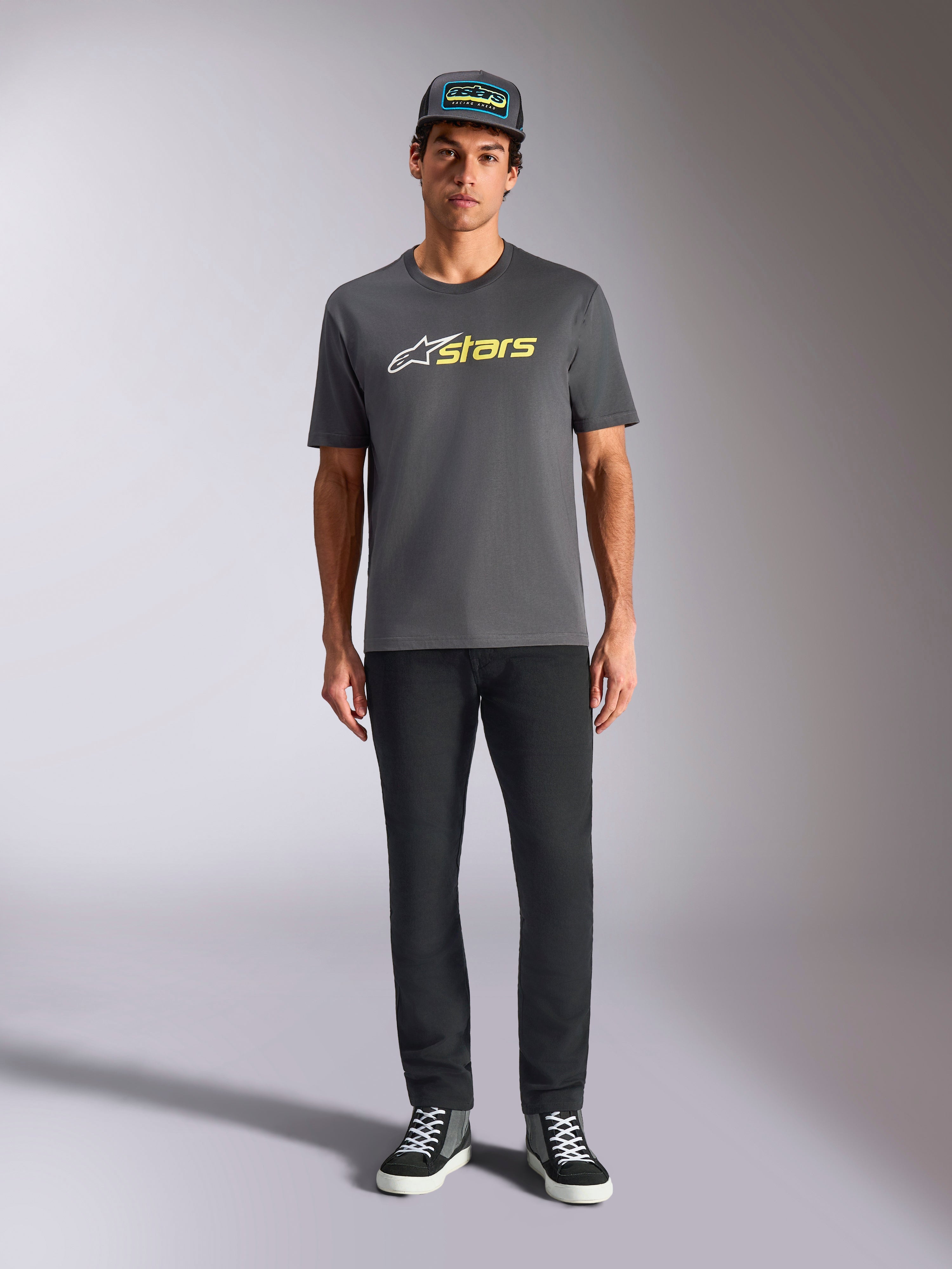 Alpinestars Blaze 2.0 CSF Tee, t-shirt met korte mouwen, antracietgrijs met wit en hi-vis geel logo, gedragen met een zwarte broek en een bijpassende truckerpet, casual motorsport lifestyle