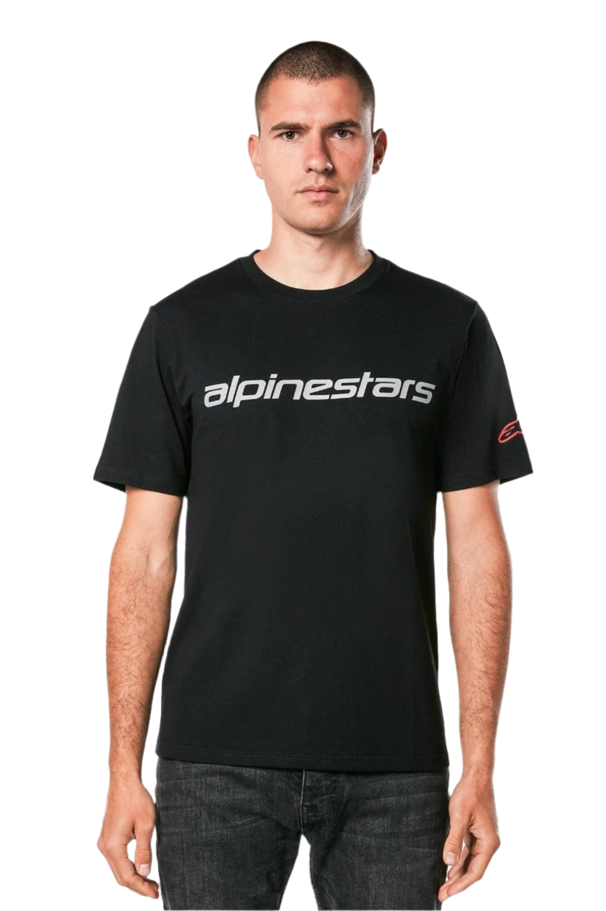 Alpinestars Linear Wordmark 2.0 CSF Tee, kurzärmeliges T-Shirt, Schwarz, graue Linear-Wortmarke auf der Brust und rotes Ageless-Logo am Ärmel, getragen von einem Model mit dunkler Jeans, lässige vom Motorsport inspirierte Streetwear