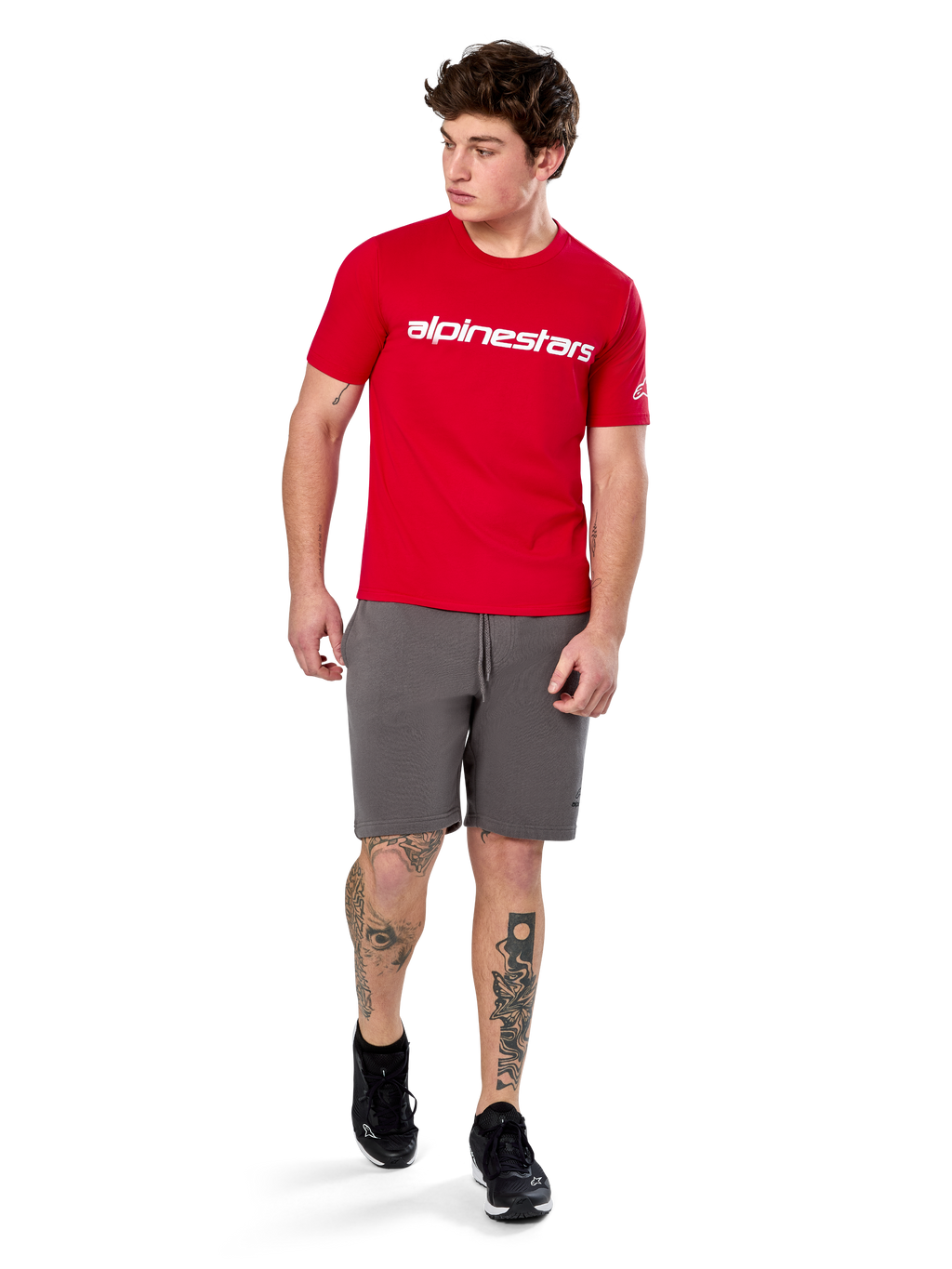 Alpinestars Linear Wordmark 2.0 CSF Tee, T-shirt met korte mouwen, rood met wit woordmerklogo op de borst, gedragen door model met grijze korte broek en zwarte sneakers, casual motorsport-geïnspireerde streetwear