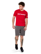 Alpinestars Linear Wordmark 2.0 CSF Tee, T-shirt met korte mouwen, rood met wit woordmerklogo op de borst, gedragen door model met grijze korte broek en zwarte sneakers, casual motorsport-geïnspireerde streetwear