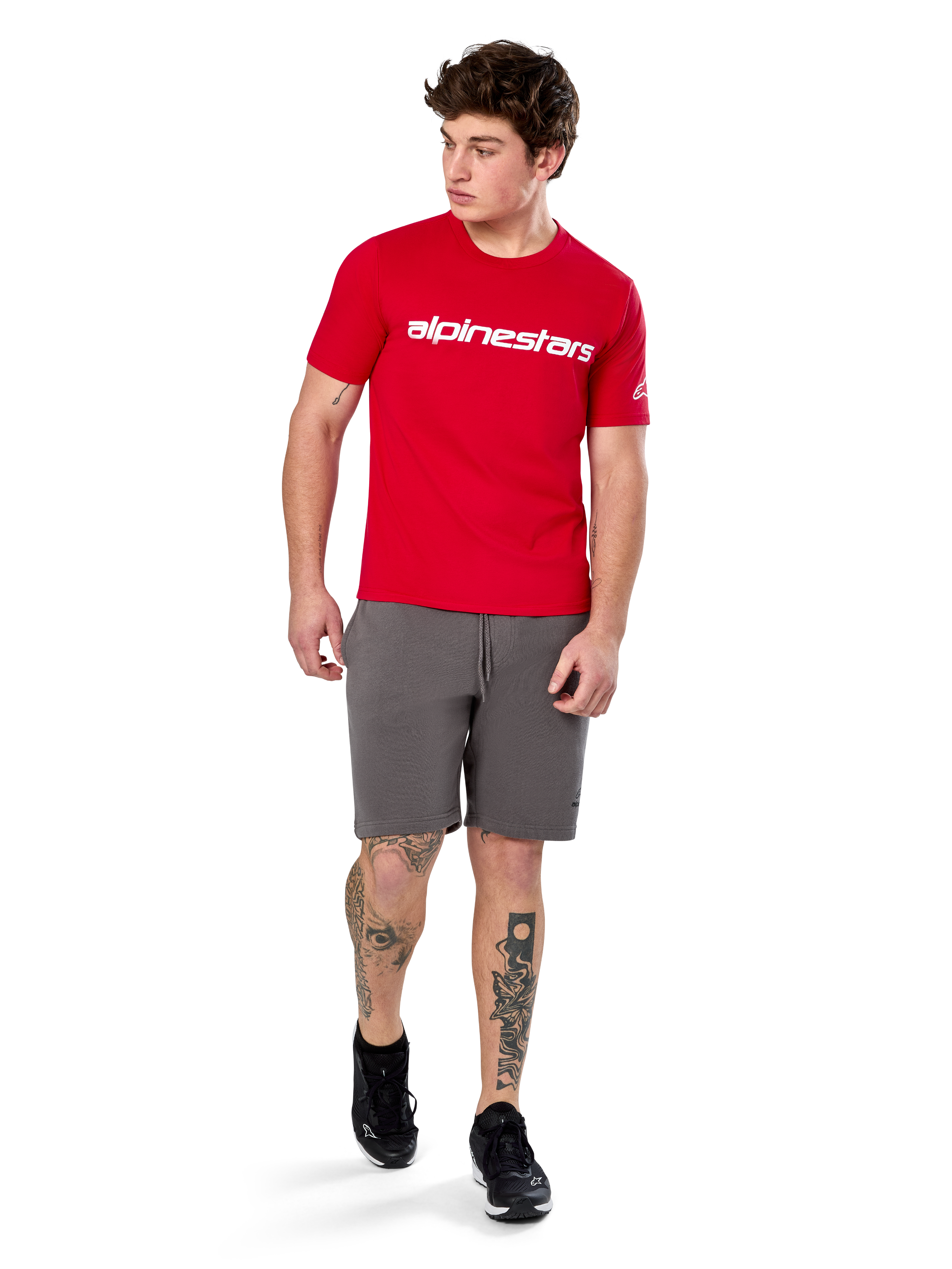 Alpinestars Linear Wordmark 2.0 CSF Tee, T-shirt met korte mouwen, rood met wit woordmerklogo op de borst, gedragen door model met grijze korte broek en zwarte sneakers, casual motorsport-geïnspireerde streetwear