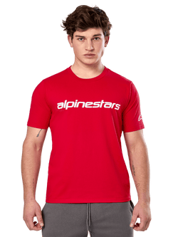 T-shirt Alpinestars Linear Wordmark 2.0 CSF, t-shirt à manches courtes, rouge, mot-symbole linéaire blanc sur la poitrine et logo Ageless sur la manche, porté par un mannequin homme avec un pantalon de survêtement gris, style streetwear décontracté inspiré du sport automobile