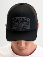 Alpinestars Heritage Patch Trucker pet, casual sportswear pet in zwart en grijs, met een gebogen klep, gestructureerde kroon, poly mesh achterkant en groot geborduurd logopatch gedragen door een persoon