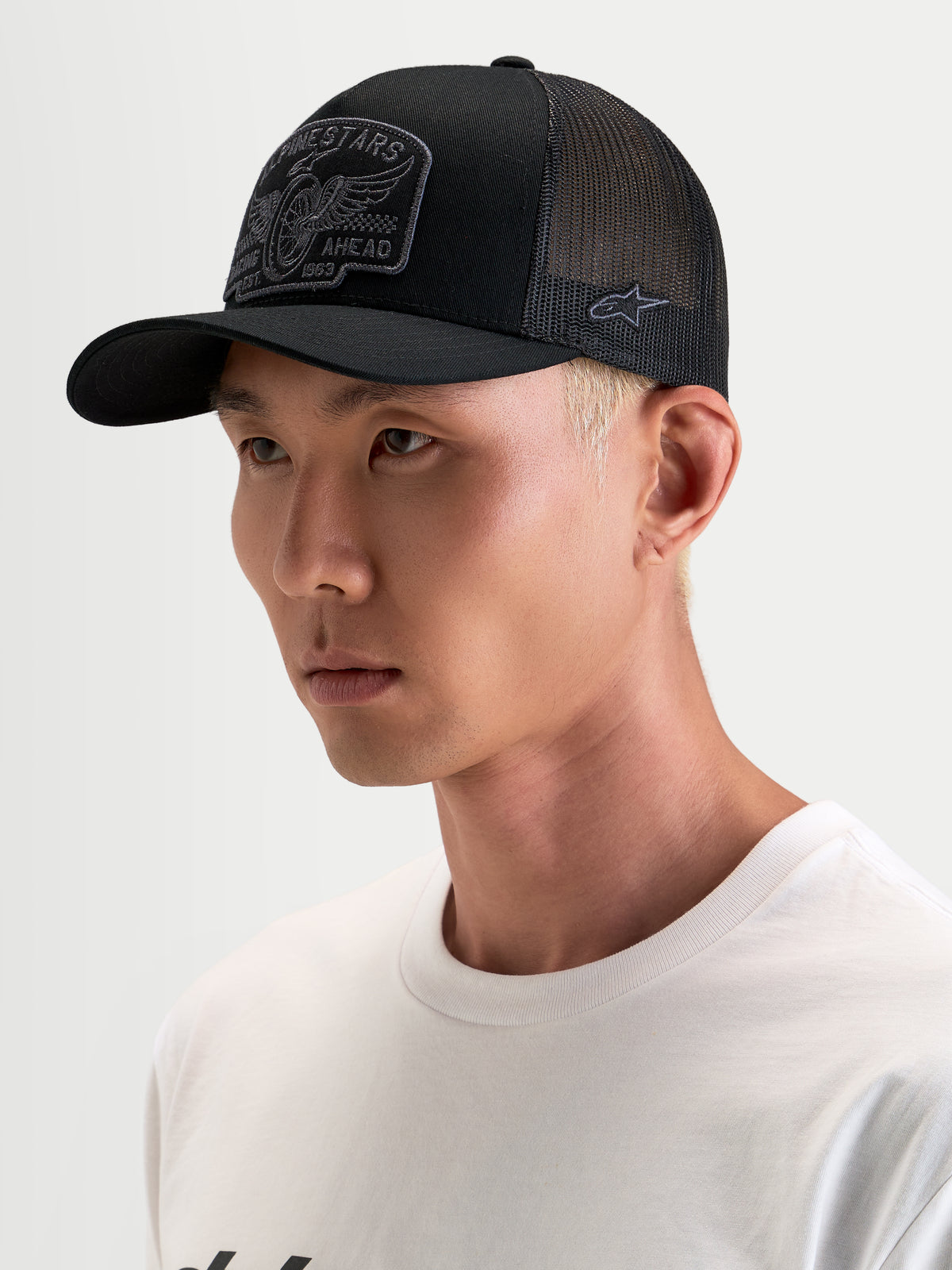 Alpinestars Heritage Patch Trucker pet, casual sportswear pet, zwart en grijs, gebogen klep en gestructureerde kroon met geborduurd patchlogo gedragen door een model