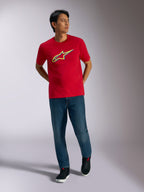 Alpinestars Ageless Shadow CSF T-shirt, rood T-shirt met korte mouwen, geel en blauw shadow logo-grafiek, gedragen met een blauwe jeans en zwarte sneakers, casual motorsport lifestyle-kleding