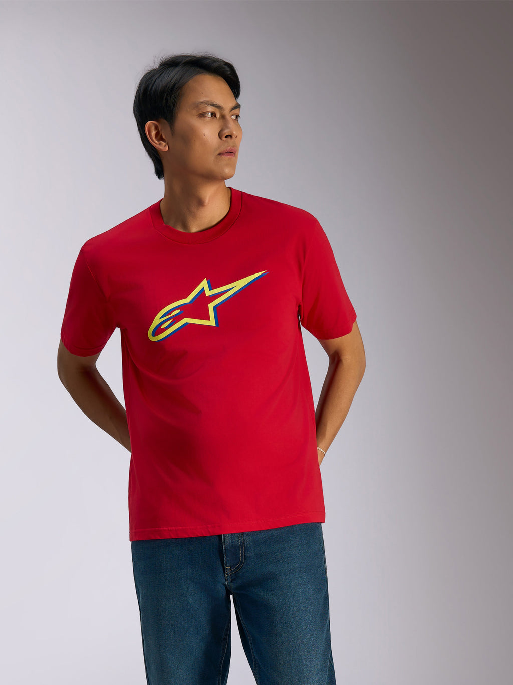 Alpinestars Ageless Shadow CSF Tee, T-shirt met korte mouwen, rood, geel en blauw schaduwlogo op de borst, casual motorsport streetwear gedragen met een blauwe jeans