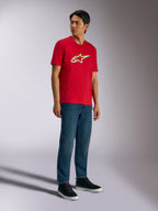 Alpinestars Ageless Shadow CSF Tee, T-shirt met korte mouwen, rood, met Ageless shadow-logo met gele en blauwe accenten, gedragen door model met denim jeans en zwarte sneakers, Casual Motorsport Streetwear