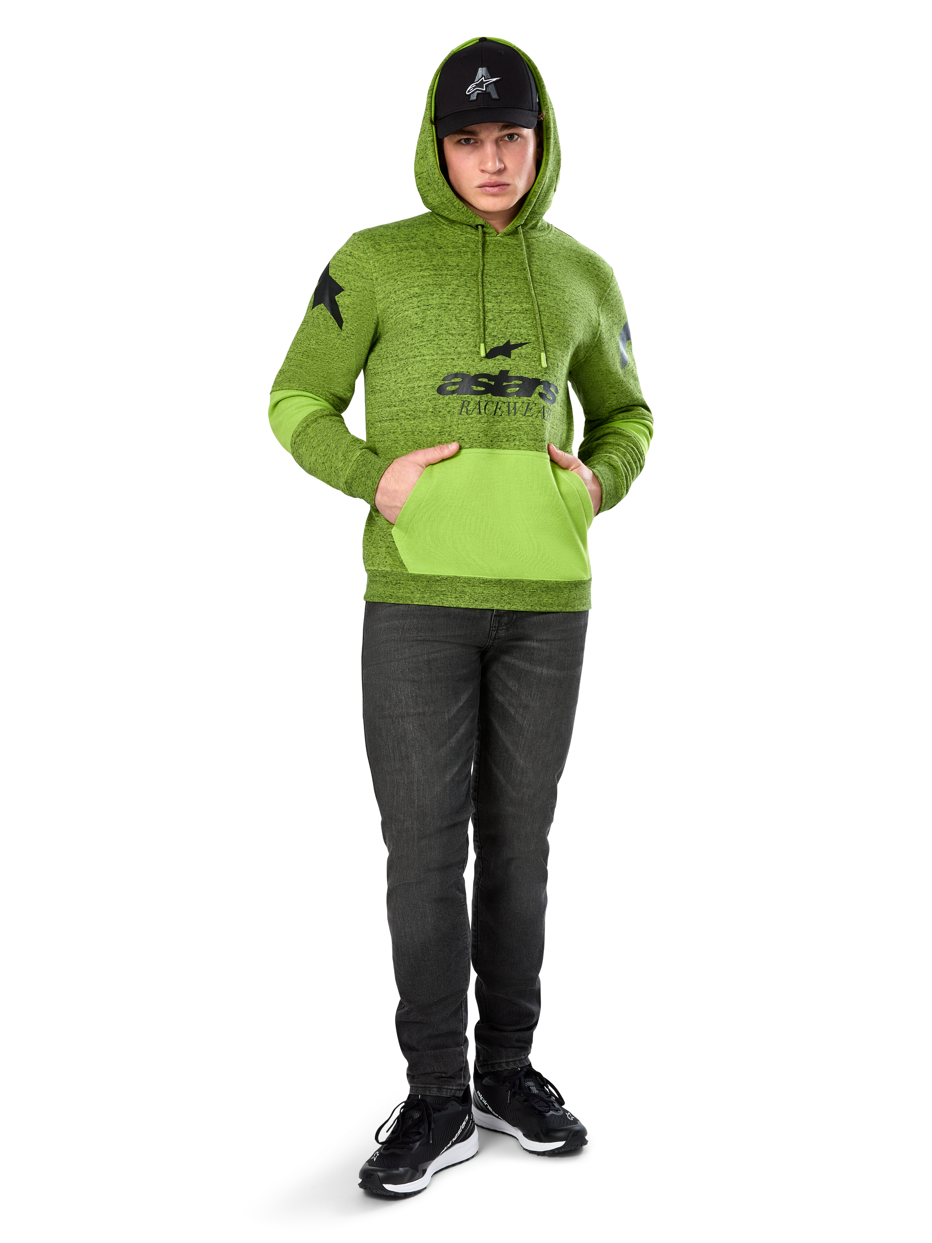 Alpinestars Perpetuate Hoodie, gemêleerde limegroene pullover fleece met contrasterende felgroene kangoeroezak en mouwpanelen, zwarte 'astars' graphic op de voorzijde, gedragen met een zwarte pet en donkere jeans, casual motorsport-geïnspireerde streetwear