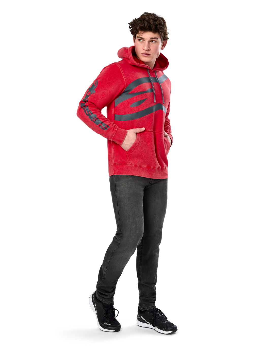 Alpinestars Unbound Hoodie, rode kledinggeverfde pullover fleece, extra groot donker logo op de borst en woordmerk op de mouwen, kangoeroezak, capuchon met trekkoord, gedragen door model met donkergrijze jeans en zwarte sneakers, casual op motorsport geïnspireerde streetwear