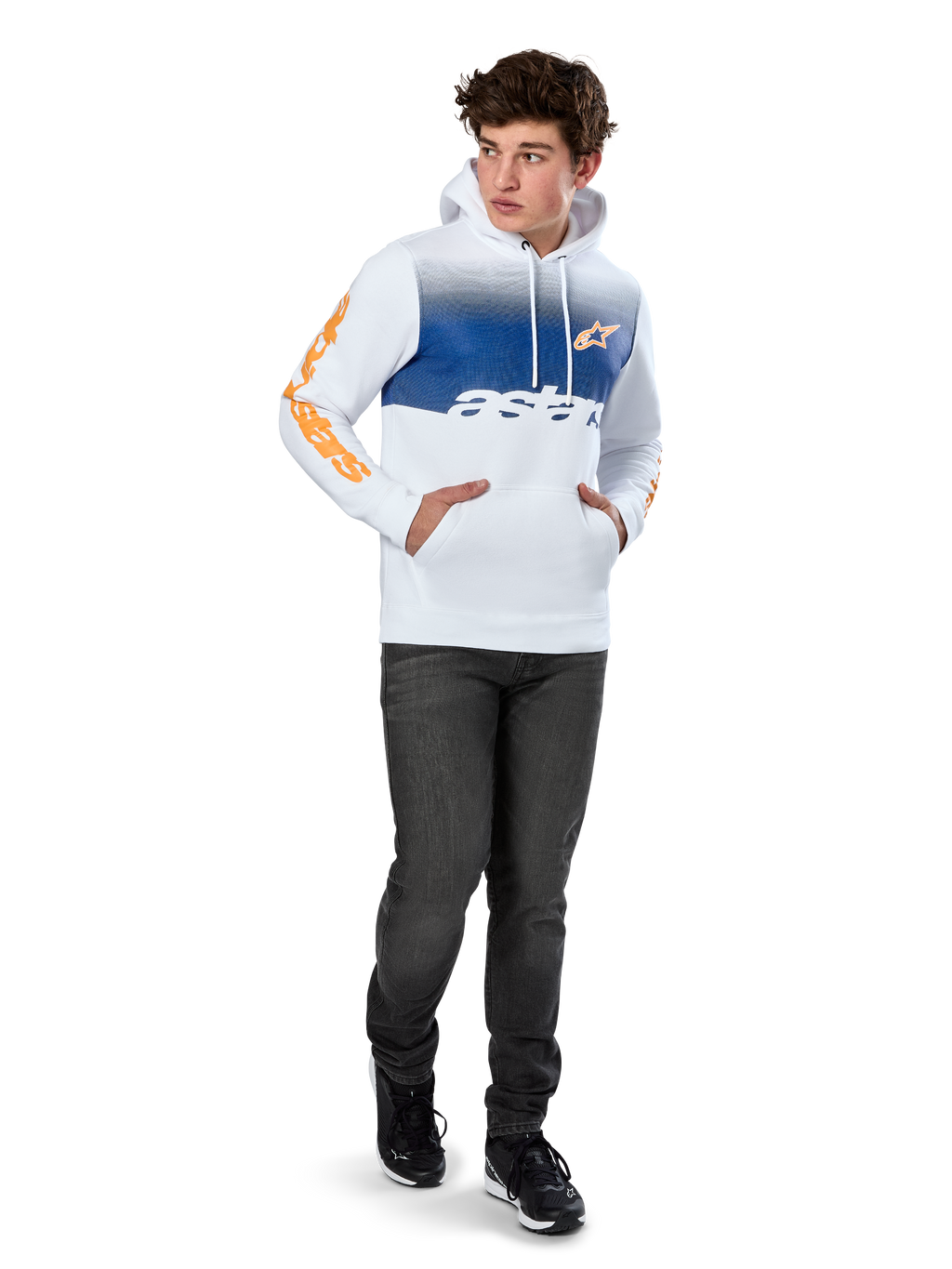 Alpinestars Specter Hoodie, witte pullover fleece met blauwe kleurverloop-print, oranje HD-logo op de borst en woordmerken op de mouwen, voorzien van een kangoeroezak en capuchon met trekkoord, gedragen met donkere jeans voor een casual motorsport-geïnspireerde look