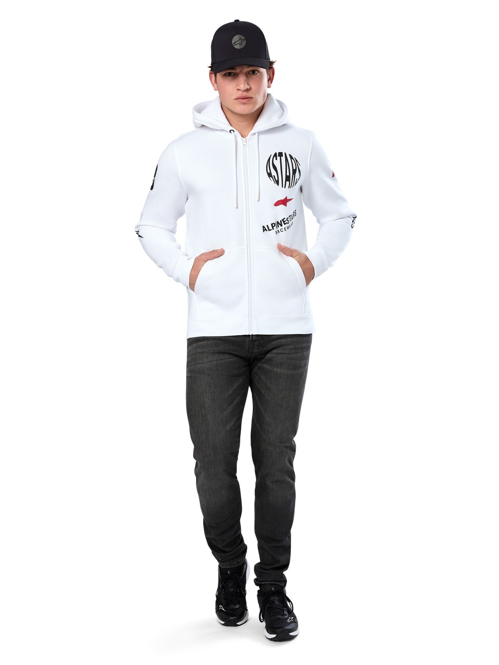 Alpinestars Variegate Hoodie, witte fleece hoodie met ritssluiting, artwork met meerdere logo's met 'ASTARS' en rood sterlogo op de borst, grafische details op de mouwen, gedragen door model met zwarte pet en zwarte jeans, casual motorsport streetwear