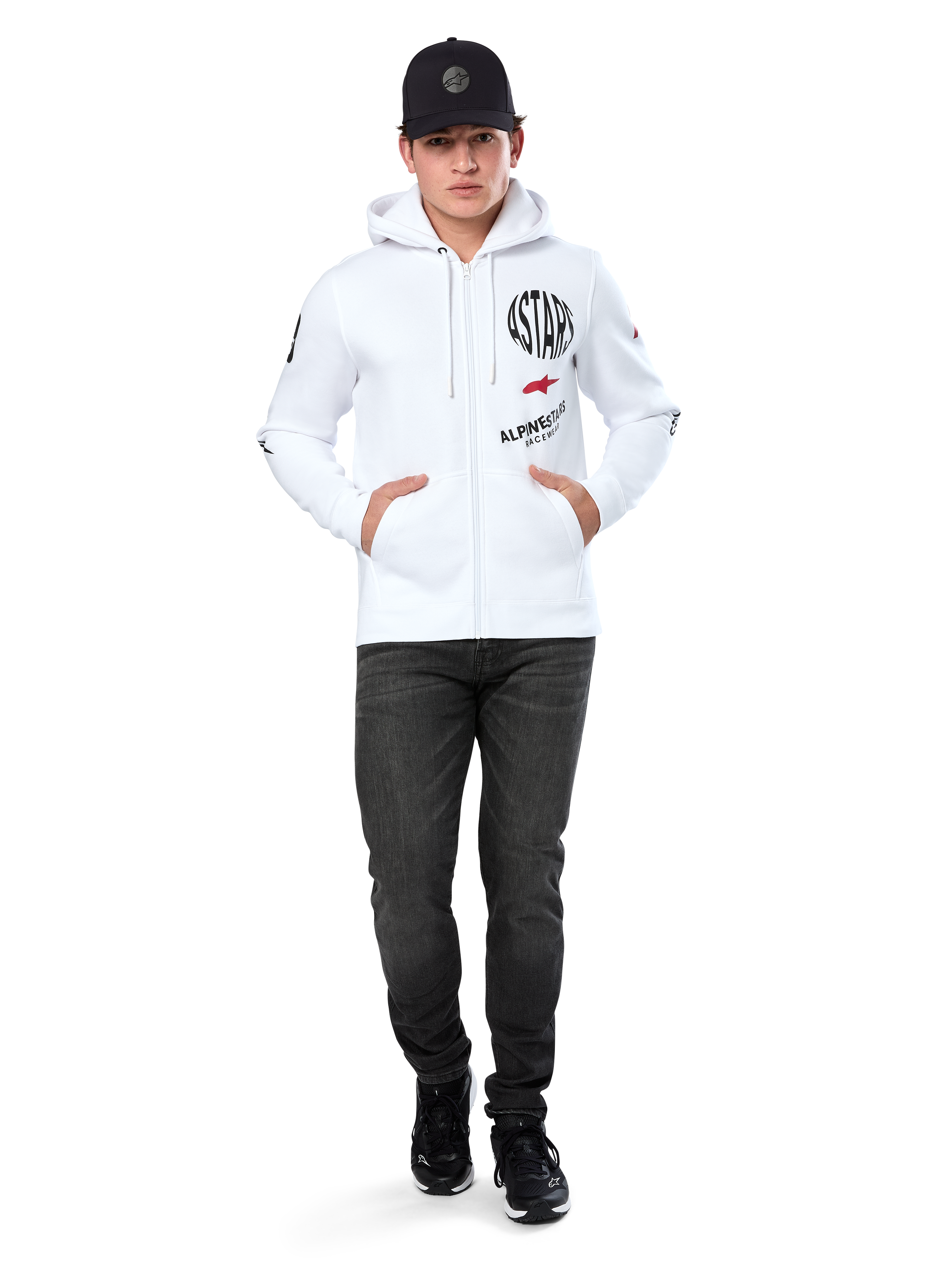 Alpinestars Variegate Hoodie, witte fleece hoodie met ritssluiting, artwork met meerdere logo's met 'ASTARS' en rood sterlogo op de borst, grafische details op de mouwen, gedragen door model met zwarte pet en zwarte jeans, casual motorsport streetwear
