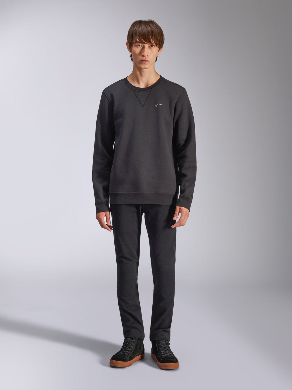 Sweatshirt Alpinestars Positive Crew, pull à col rond noir décontracté, petit logo blanc sur la poitrine, encolure avec surpiqûre en V, photo de studio en pied avec un mannequin portant un pantalon noir et des baskets, vêtements lifestyle d'inspiration motorsport