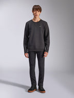 Sweatshirt Alpinestars Positive Crew, pull à col rond noir décontracté, petit logo blanc sur la poitrine, encolure avec surpiqûre en V, photo de studio en pied avec un mannequin portant un pantalon noir et des baskets, vêtements lifestyle d'inspiration motorsport