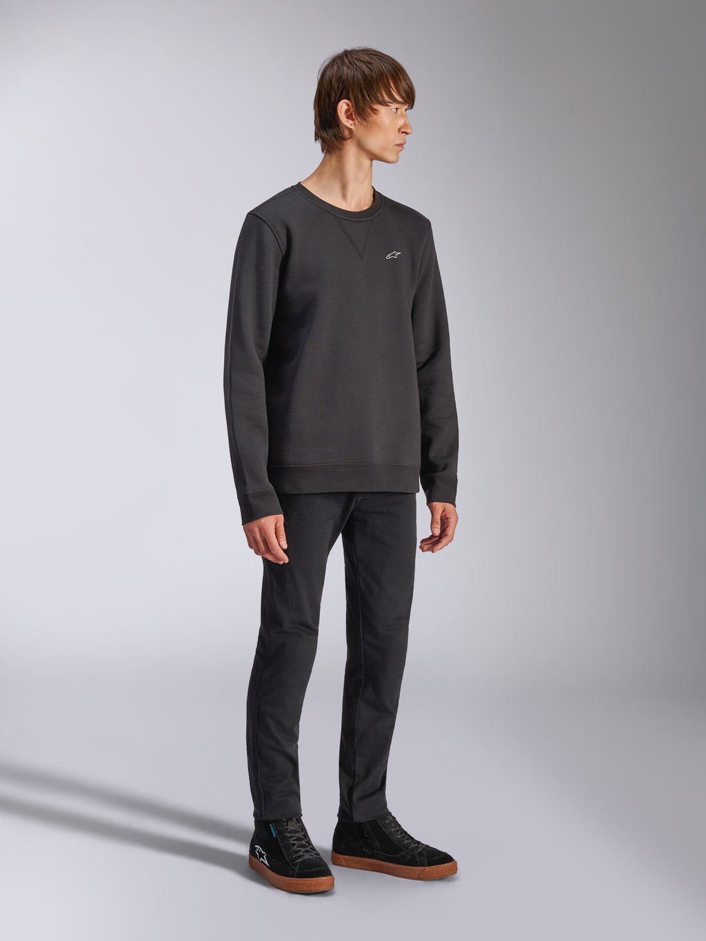 Alpinestars Positive Crew, sweat-shirt à col rond, noir, petit logo Alpinestars blanc sur la poitrine, col côtelé avec détail de couture en V, poignets et ourlet côtelés, porté par un mannequin avec un pantalon noir et des baskets, streetwear décontracté inspiré du sport automobile