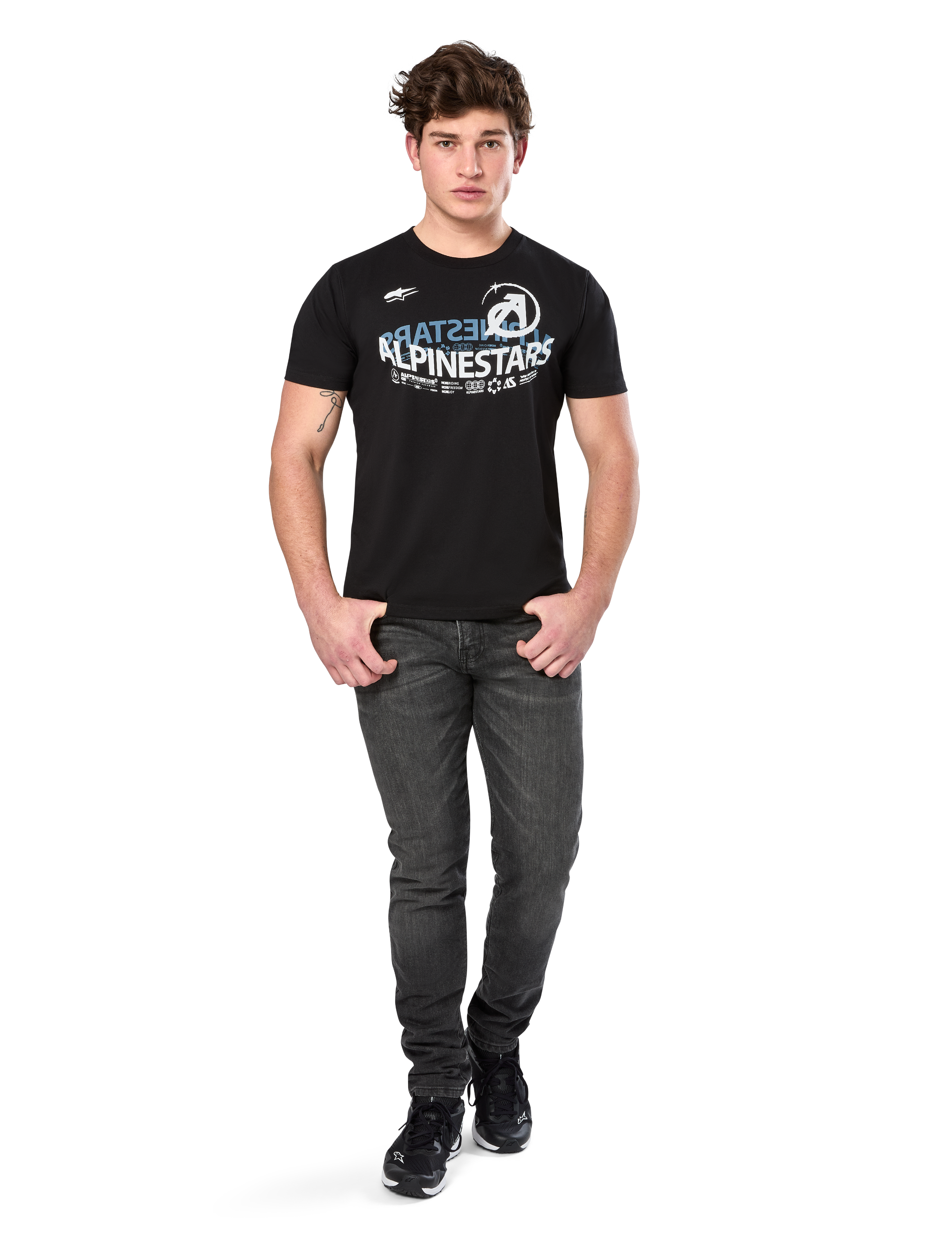 Alpinestars Semicircle CSF Tee, T-shirt met korte mouwen, zwart, wit en lichtblauw gebogen grafisch ontwerp op de borst, gedragen door model met donkergrijze jeans en zwarte sneakers, casual motorsport streetwear